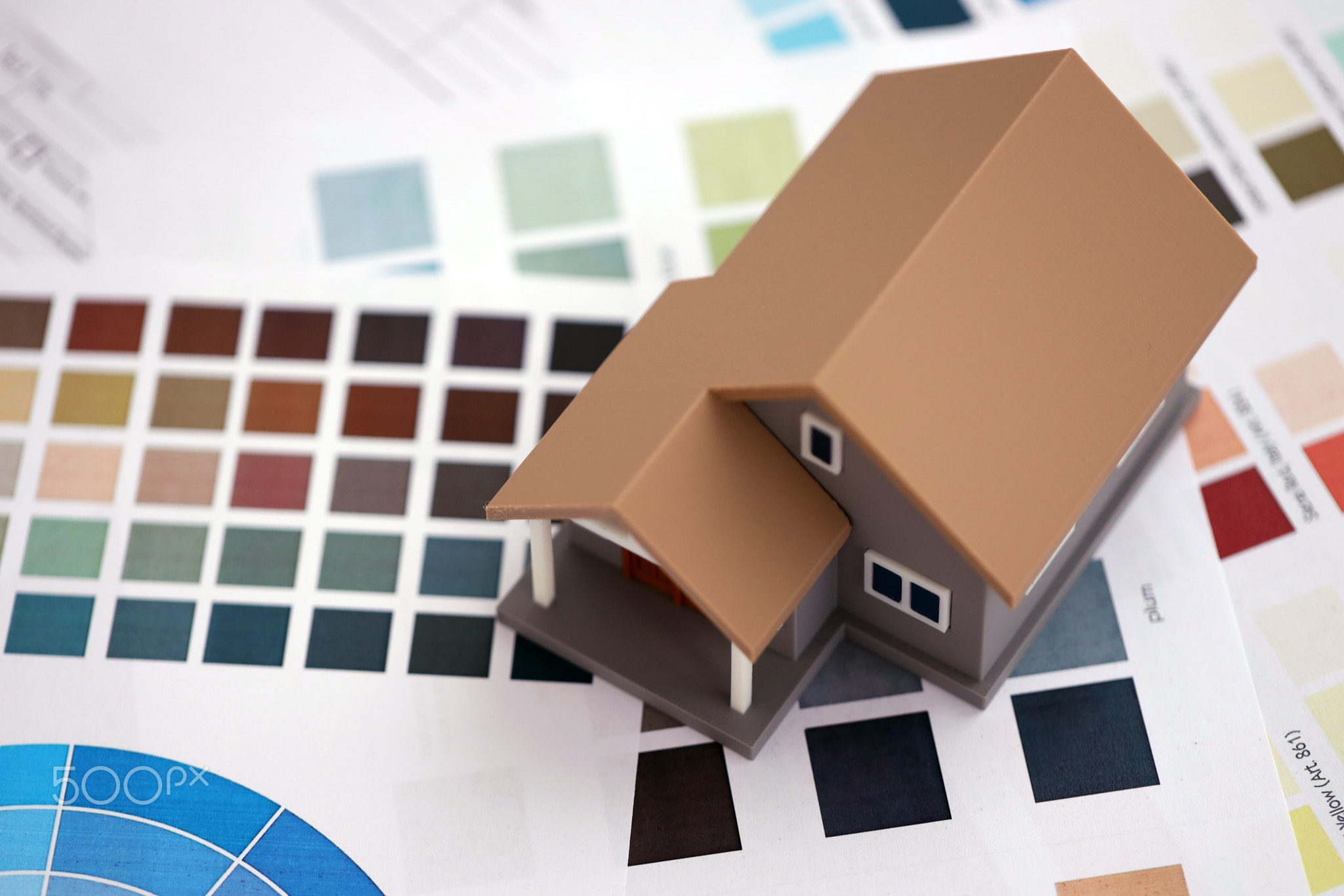 Small toy house and papers with color palette samples. Concept of interior and exterior design