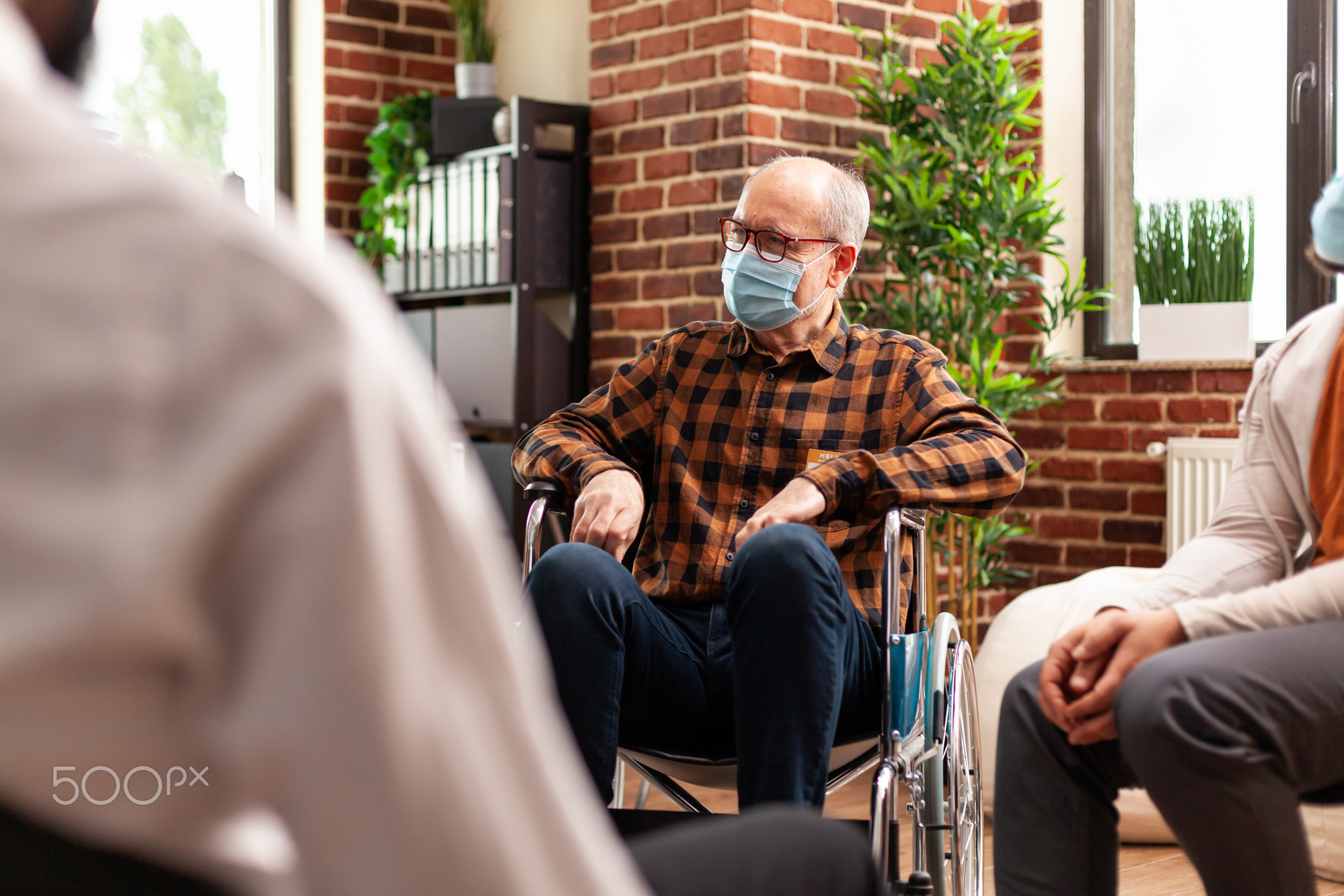 Senior man with face mask sitting in wheelchair at group therapy session