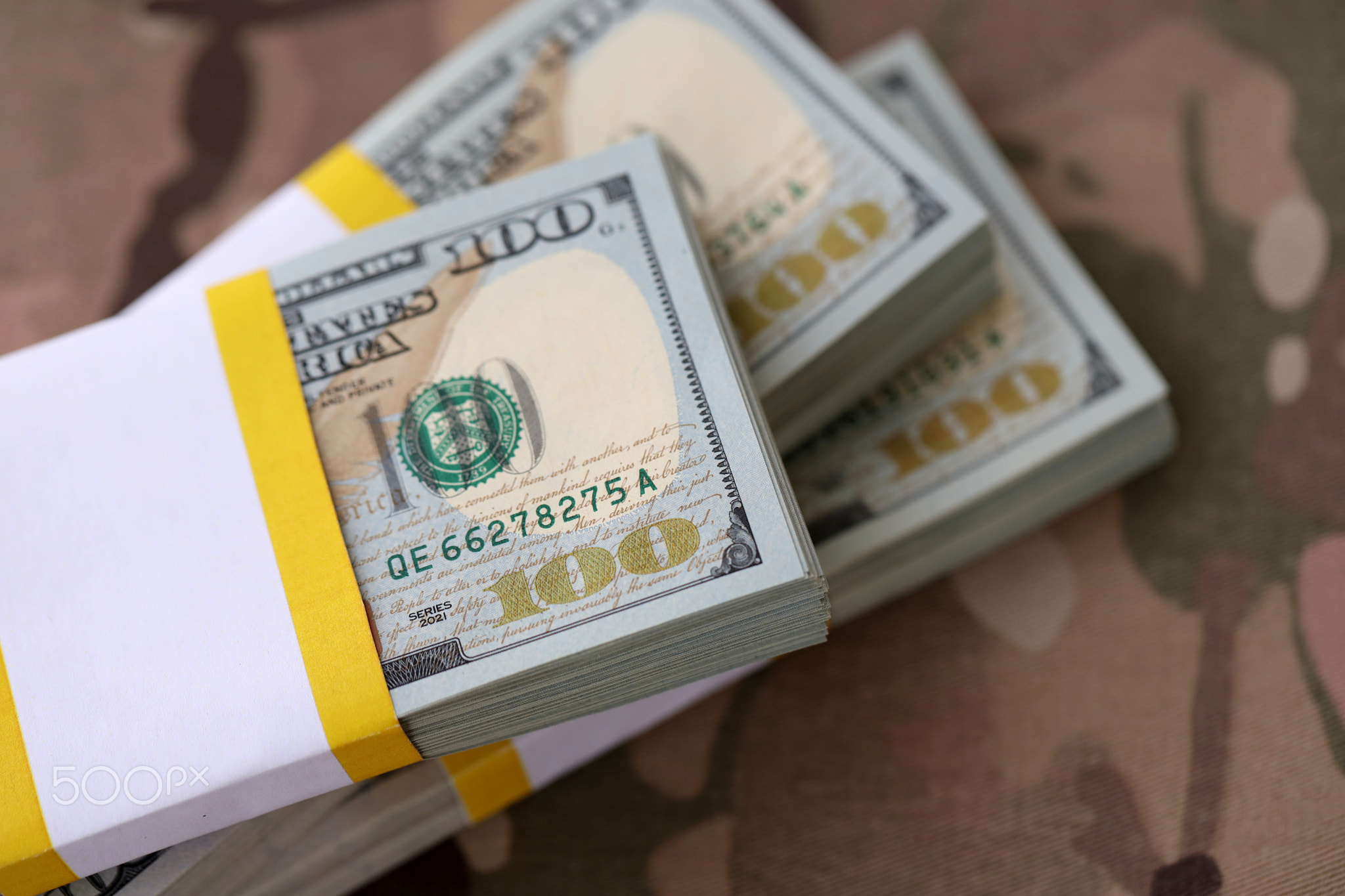 Three packs of ten thousand US dollar bills on camouflage background. Packs of hundred dollar bills