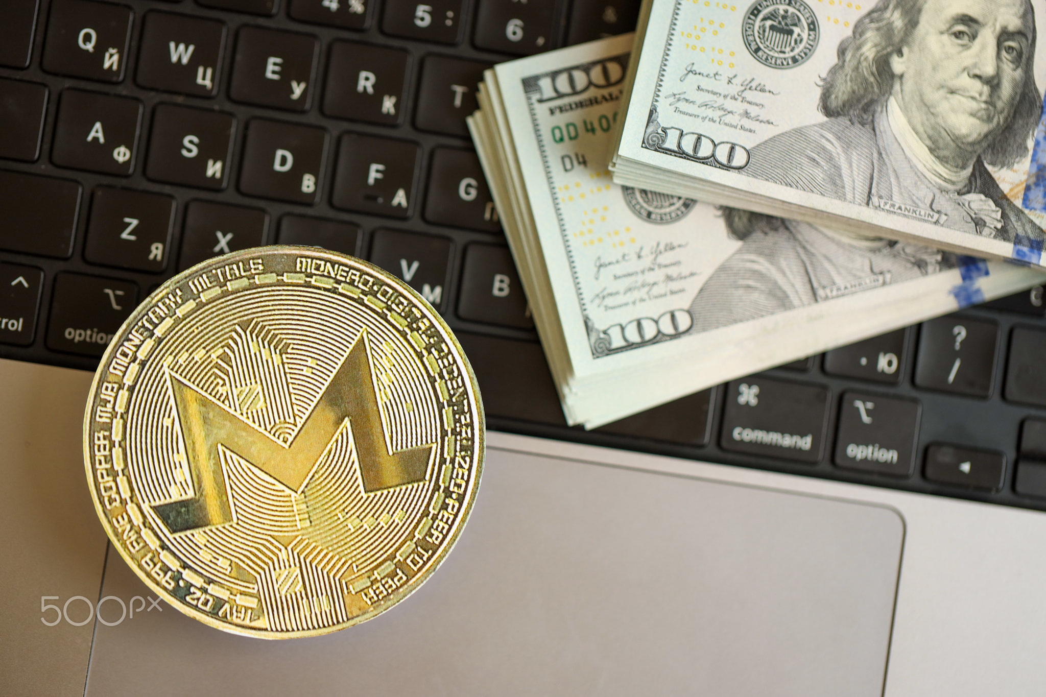 Monero XMR coin with big amount of hundred US dollar bills on laptop surface