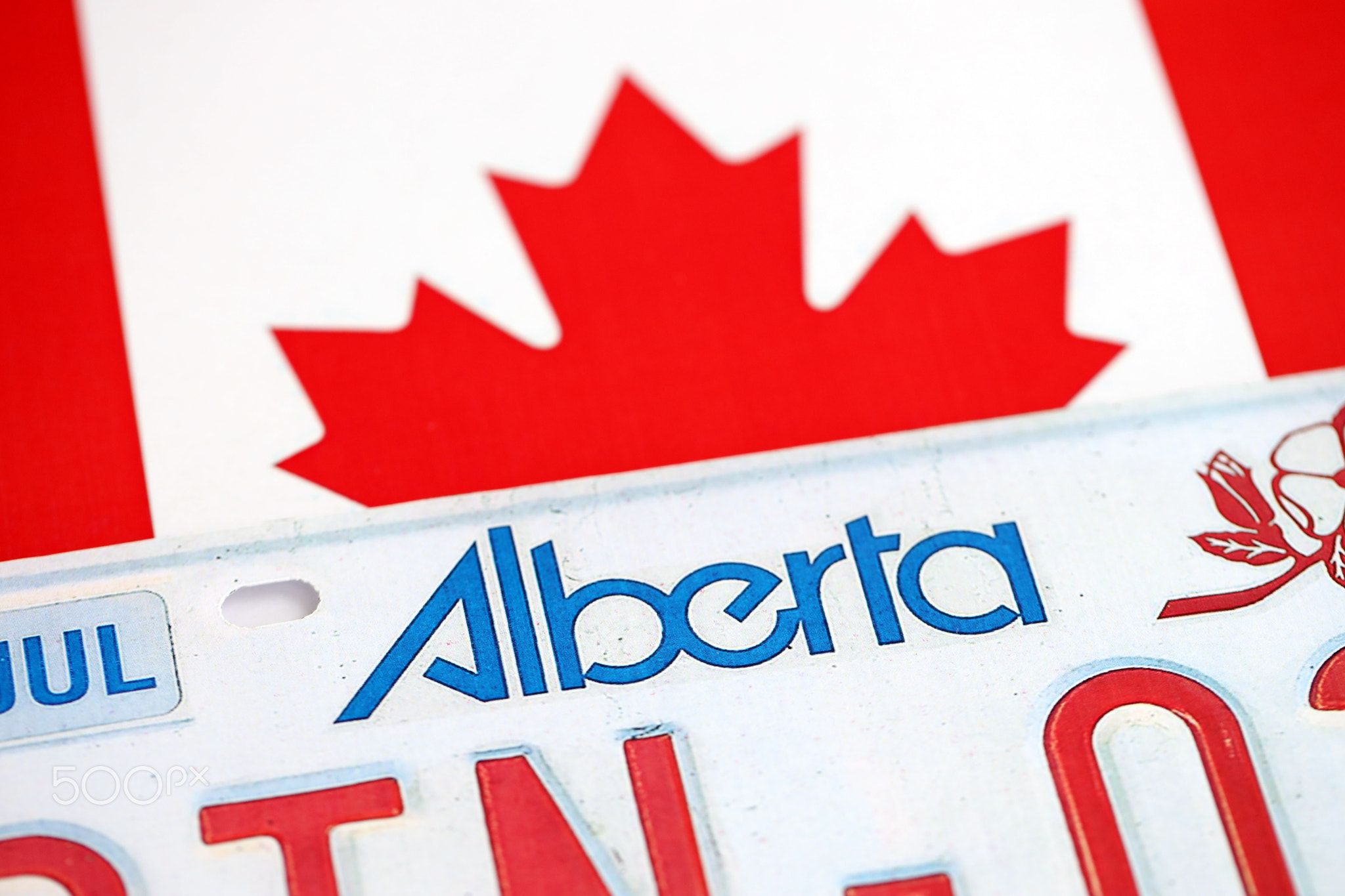 Alberta canadian car license plate on flag of Canada close up. Driving permit and registration