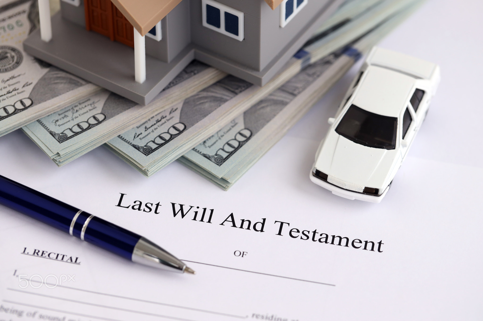 Generic toy house with US dollar bills, car and Last will and testament with pen on table