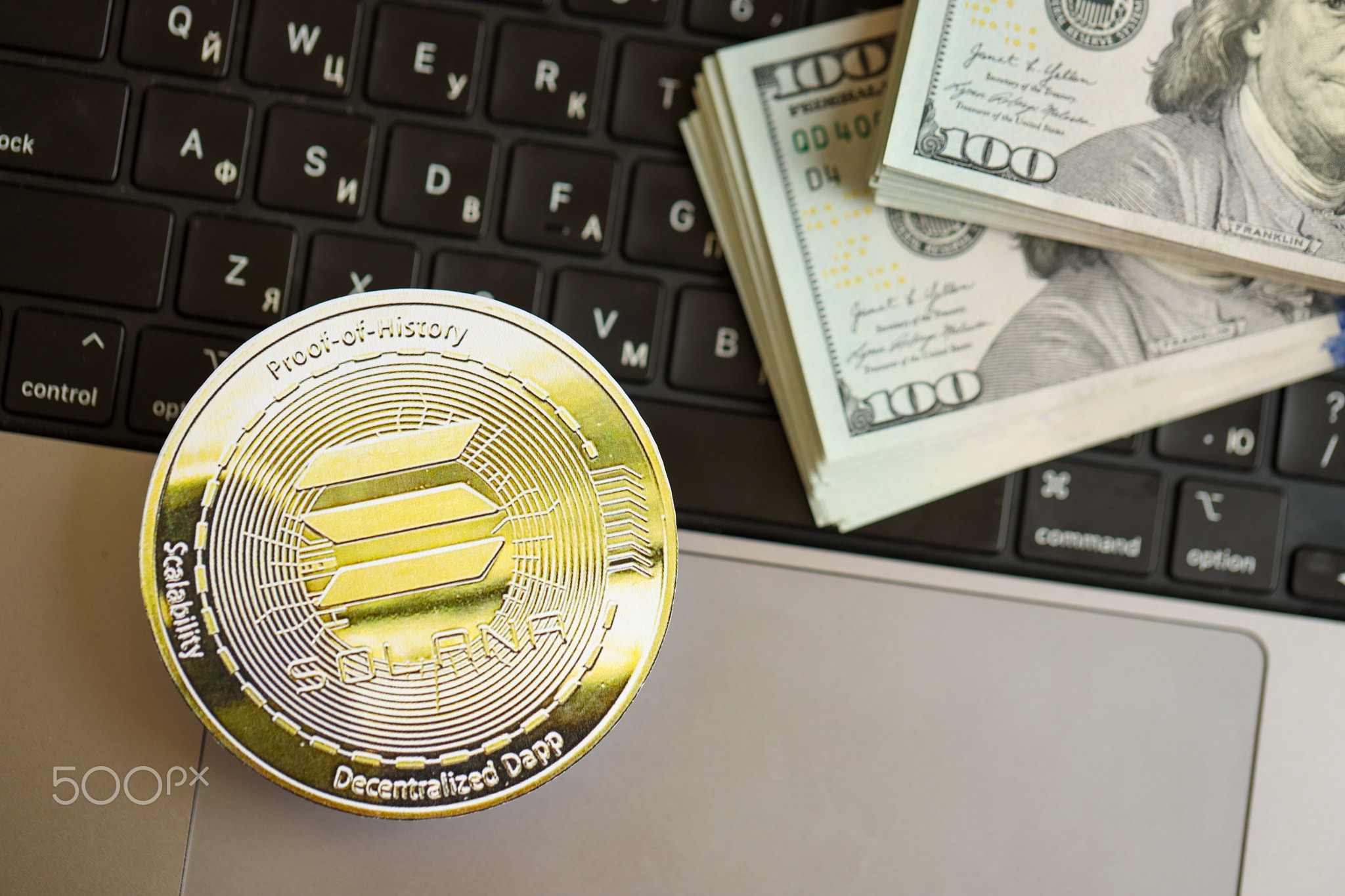 Solana SOL coin with big amount of hundred US dollar bills on laptop surface