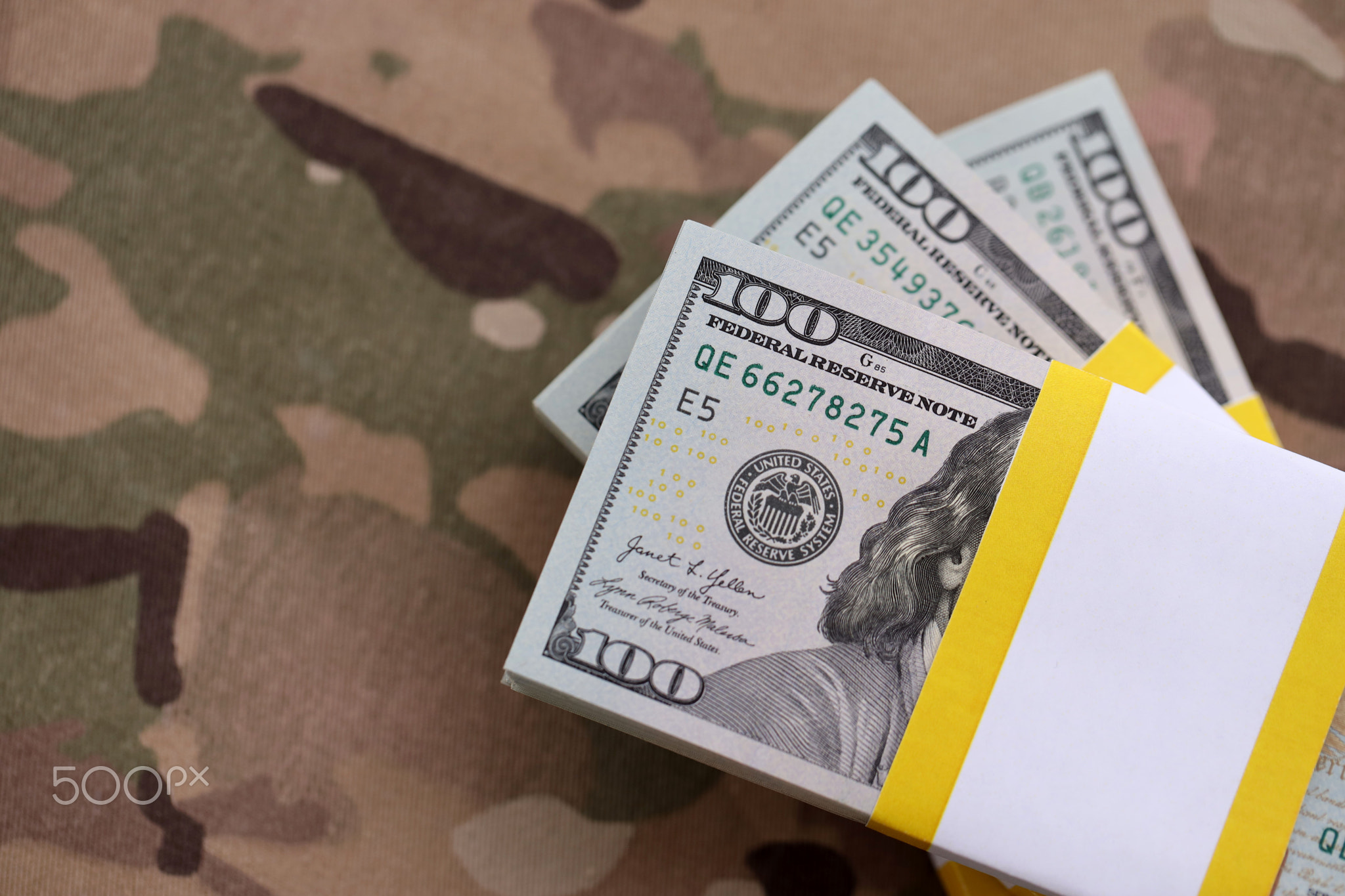 Three packs of ten thousand US dollar bills on camouflage background. Packs of hundred dollar bills
