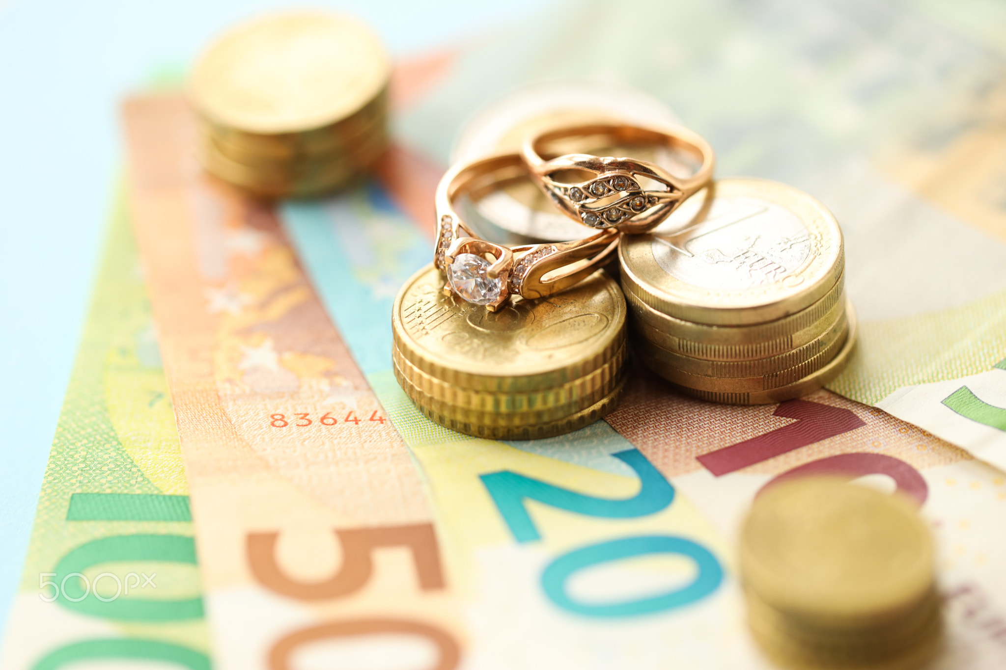 European union Euro money bills and coins with wedding rings on blue table
