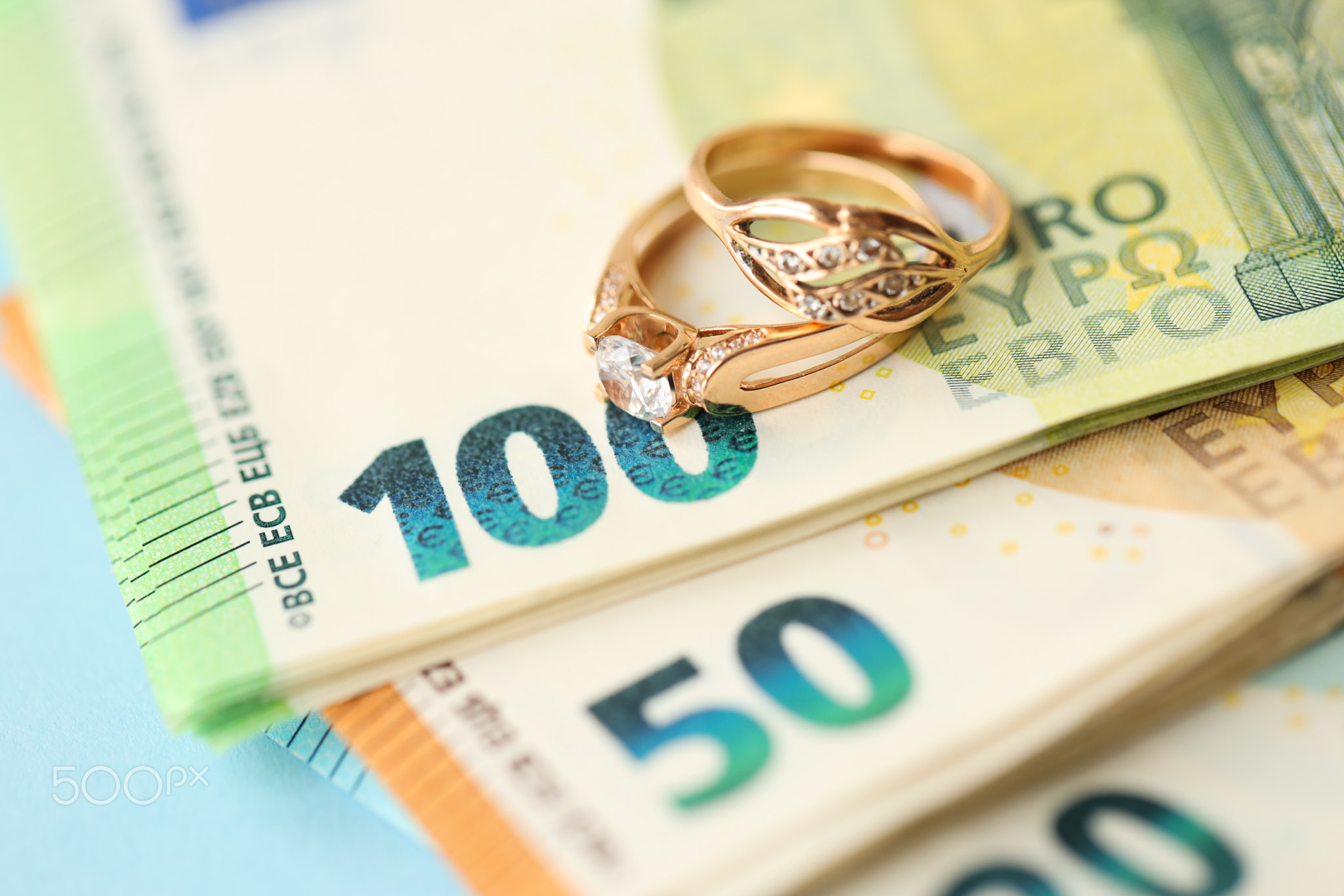 European union Euro money bills and coins with wedding rings on blue table