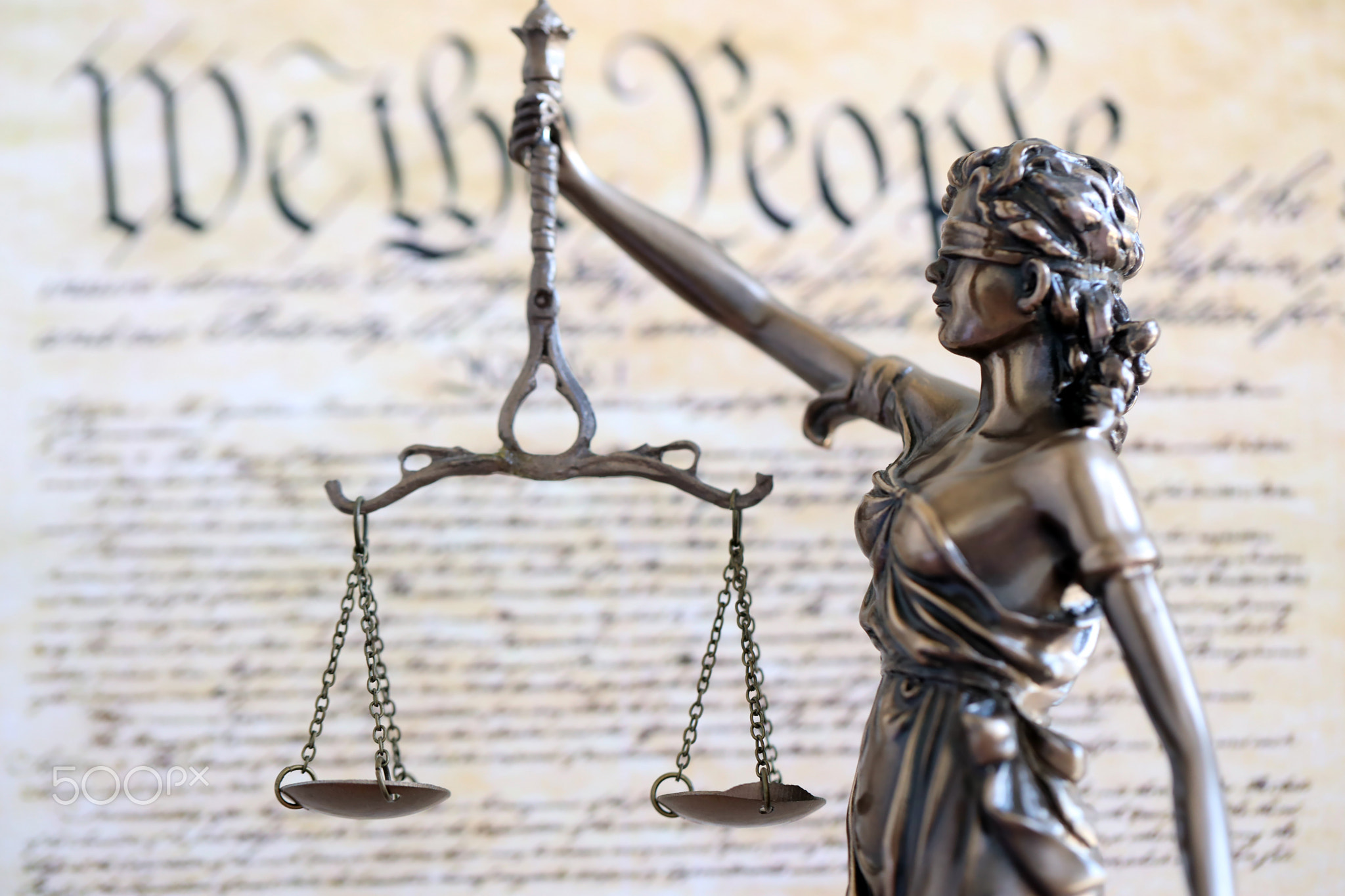 Lady Justice statue with scales on background of US Constitution. Lawsuit and punishment in US