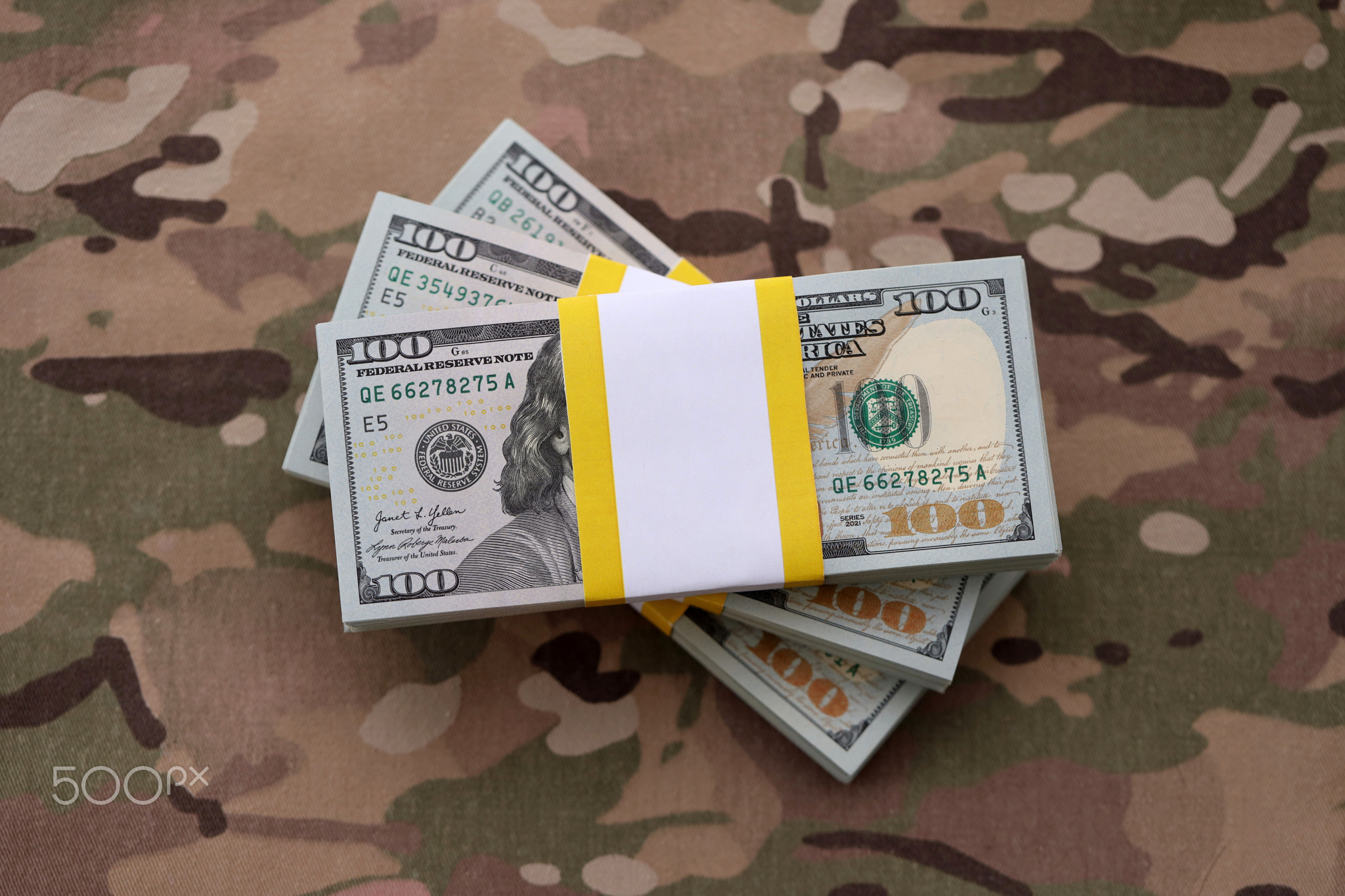 Three packs of ten thousand US dollar bills on camouflage background. Packs of hundred dollar bills