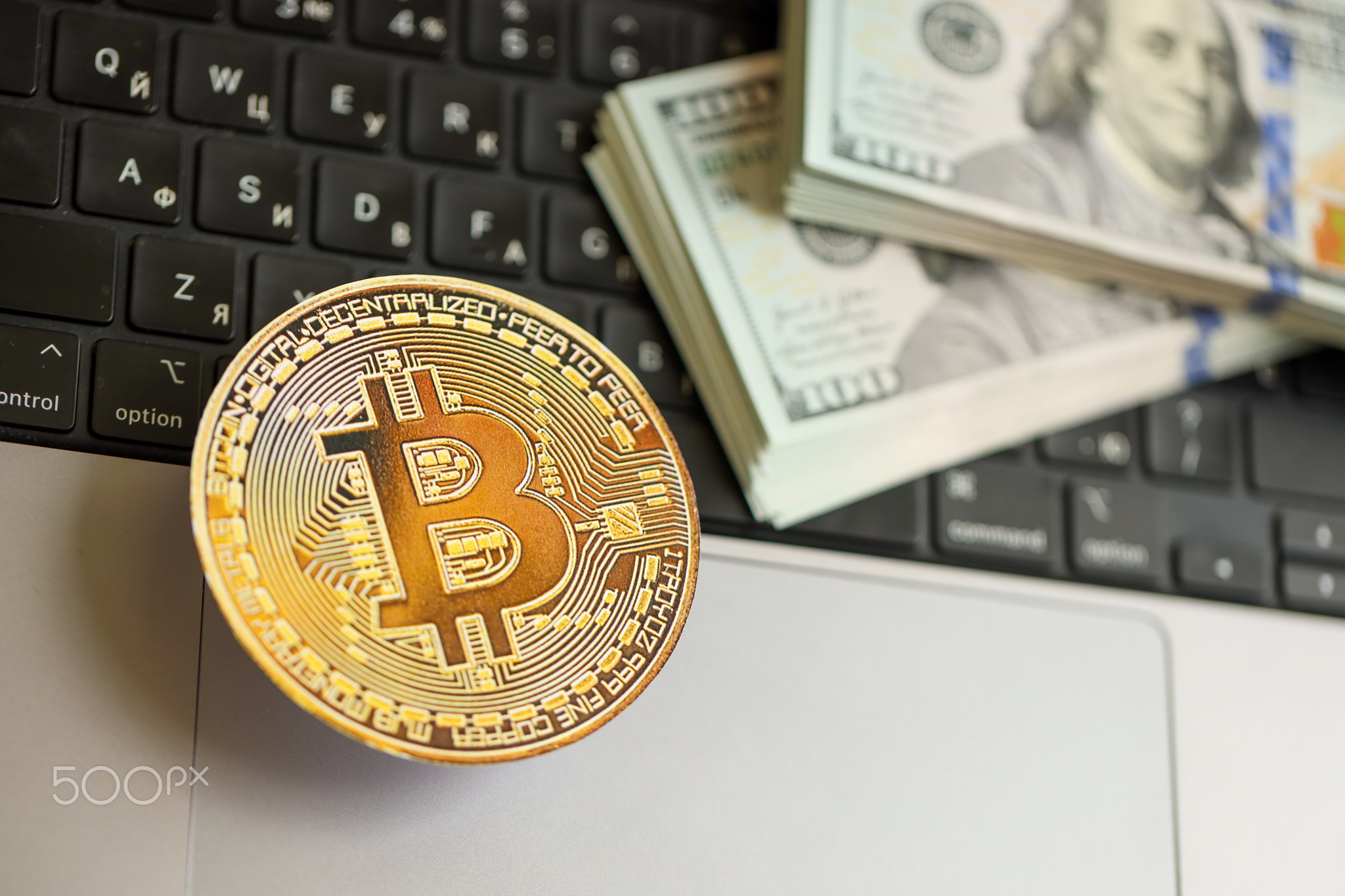 Bitcoin BTC coin with big amount of hundred US dollar bills on laptop surface