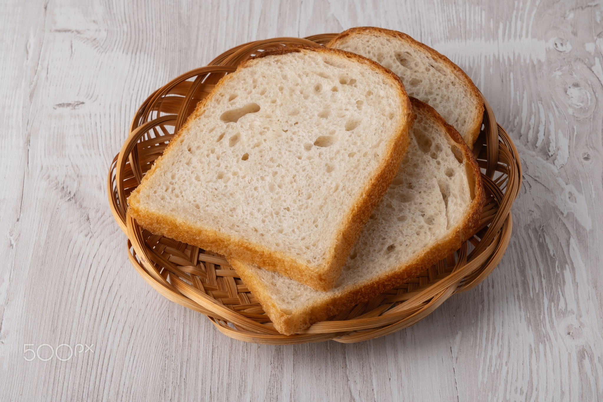 Slices of bread served in a round basket on a wooden table