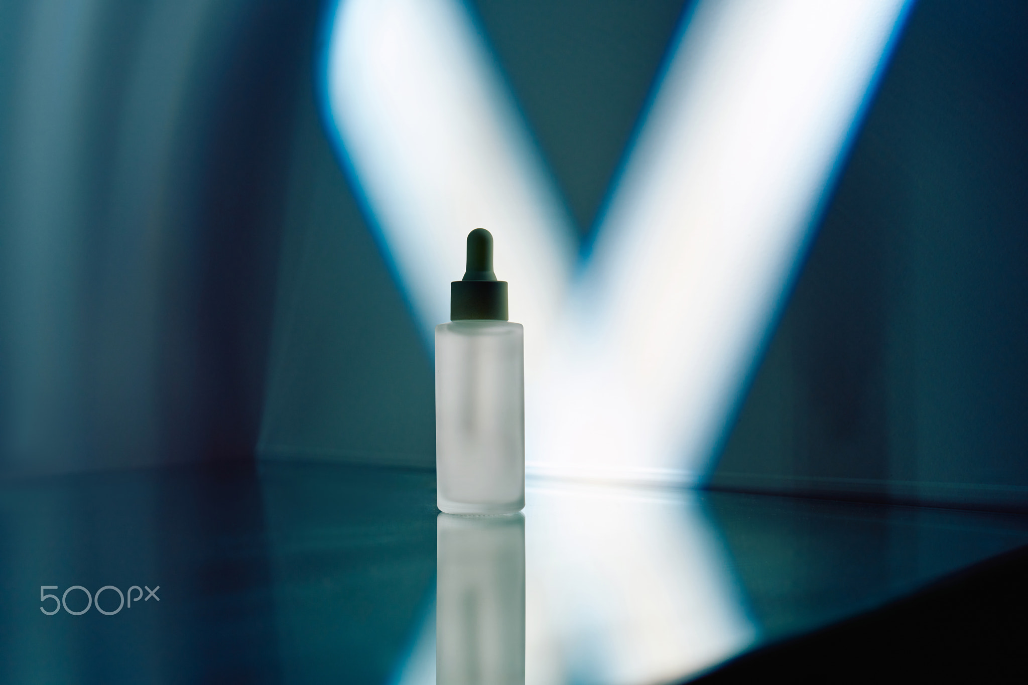 Serum dropper bottle reflecting blue light on sleek surface