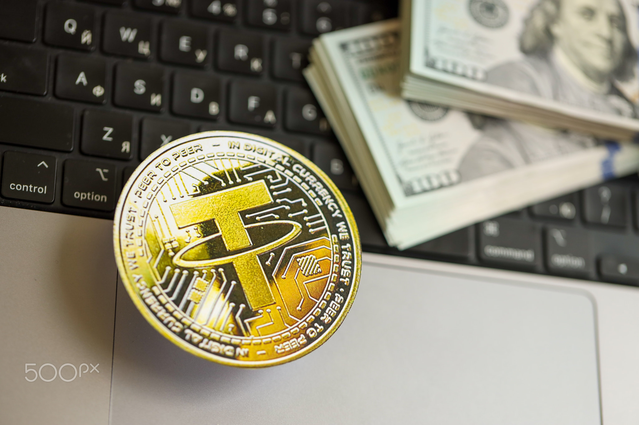 Tether USDT coin with big amount of hundred US dollar bills on laptop surface