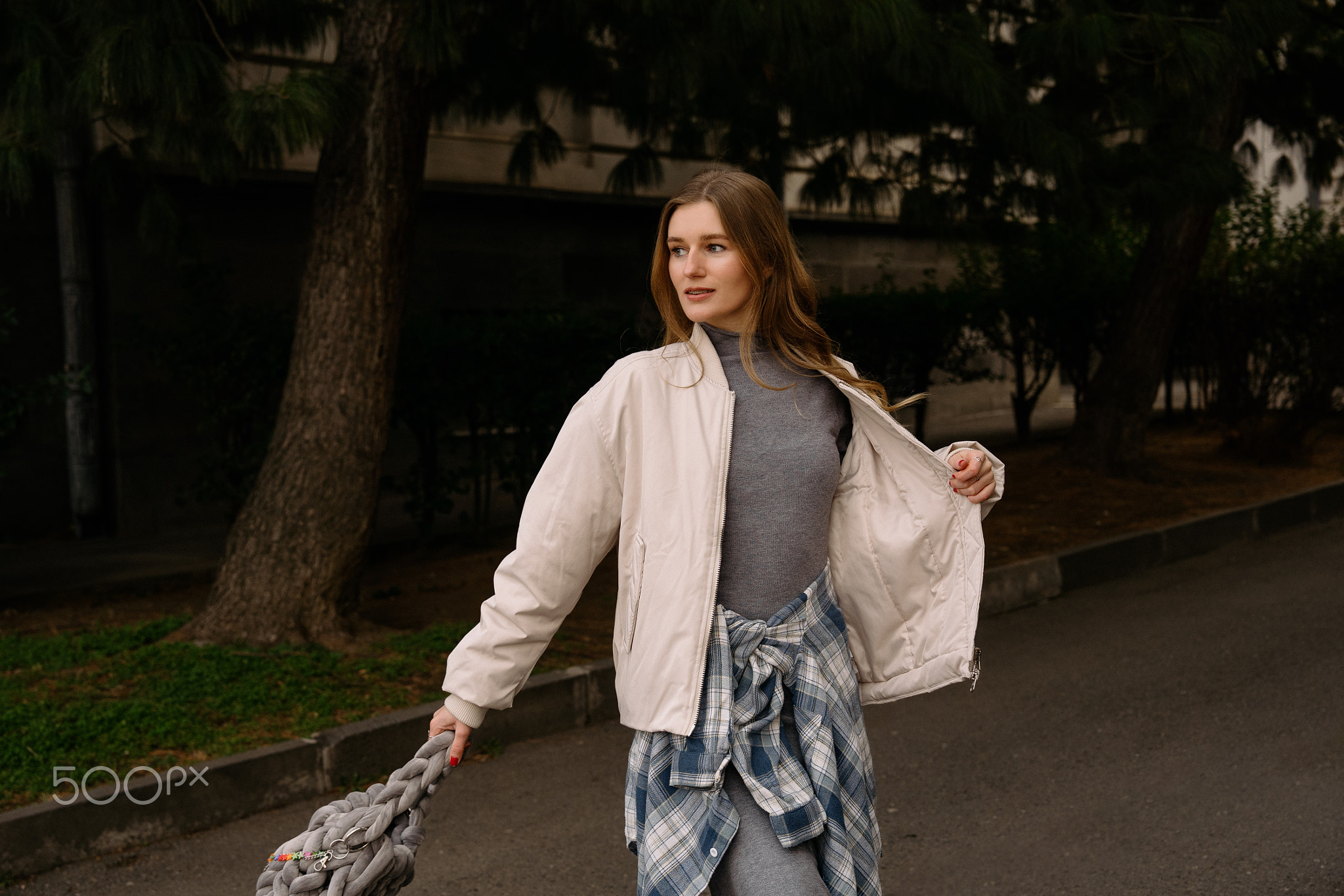 Young woman walks down street holding bag in city during daytime in casual clothing