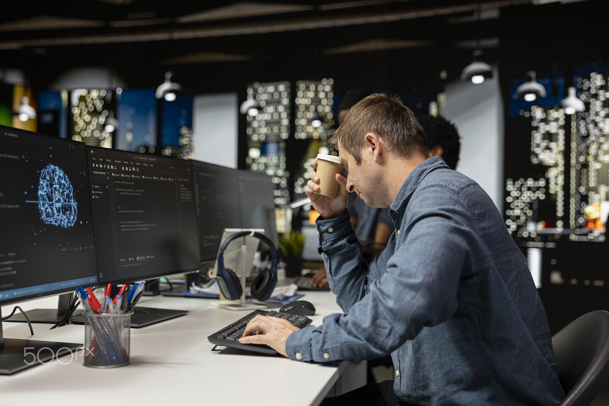Tired man drinks coffee while utilizing AI on computer to optimize performance: Tired man drinks coffee while utilizing AI on computer to optimize performance. Exhausted worker enjoys caffeinated beverage in tech company office while training deep learning models
