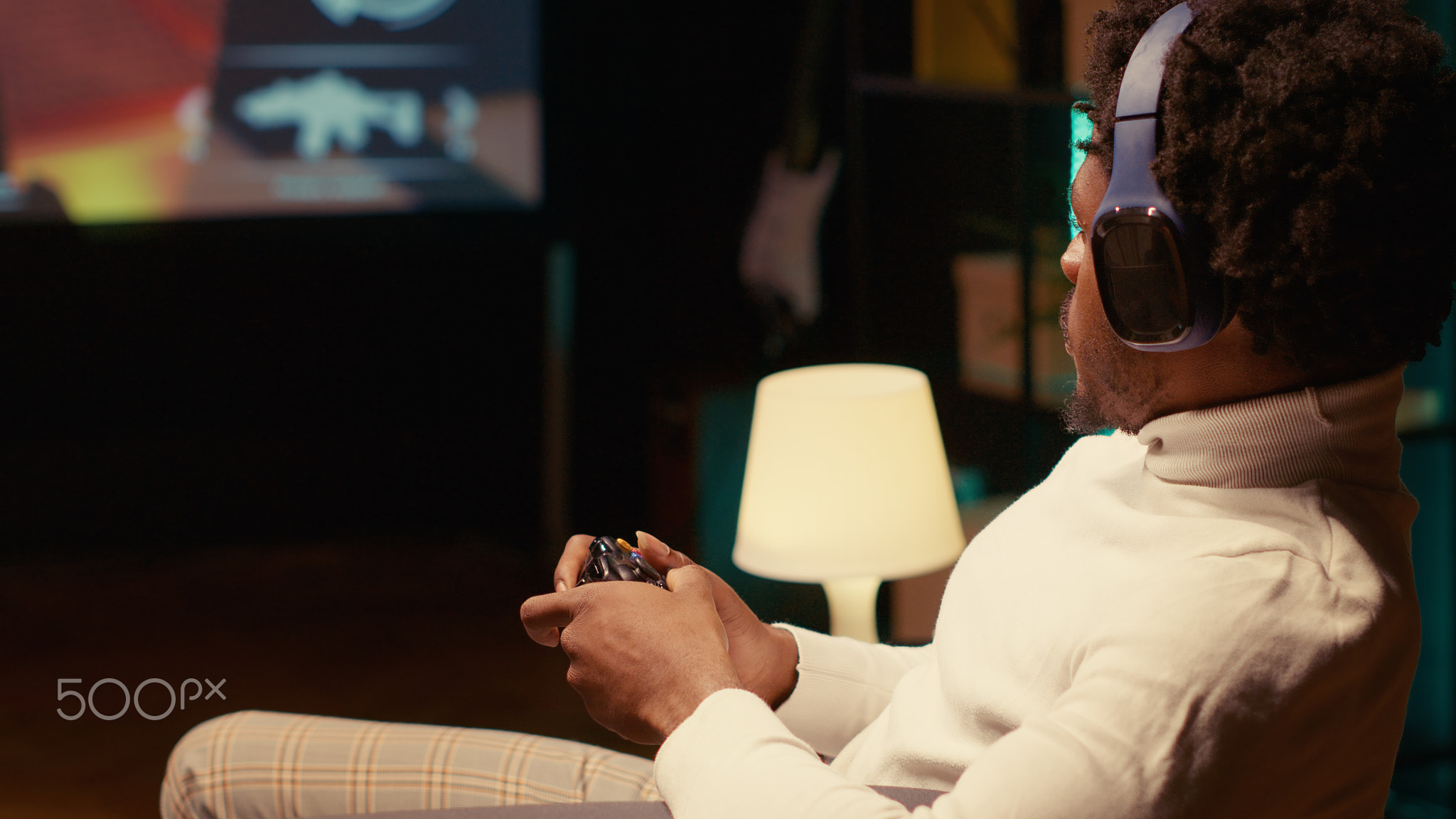 Gamer playing game on ultrawide smart TV, communicating with teammates using headphones