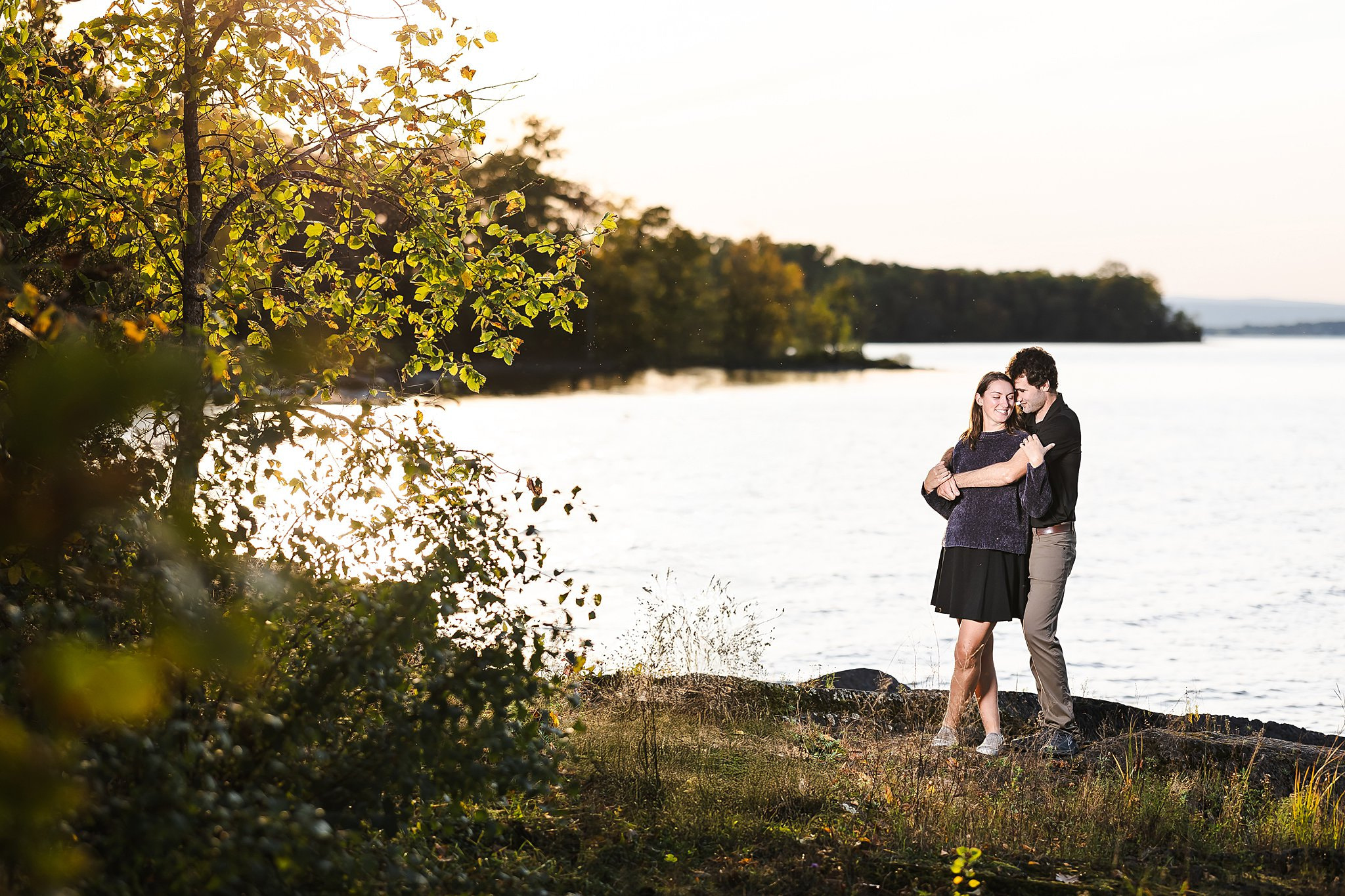 A couple embracing on a rocky shoreline during a professional Vermont engagement photography session at sunset.