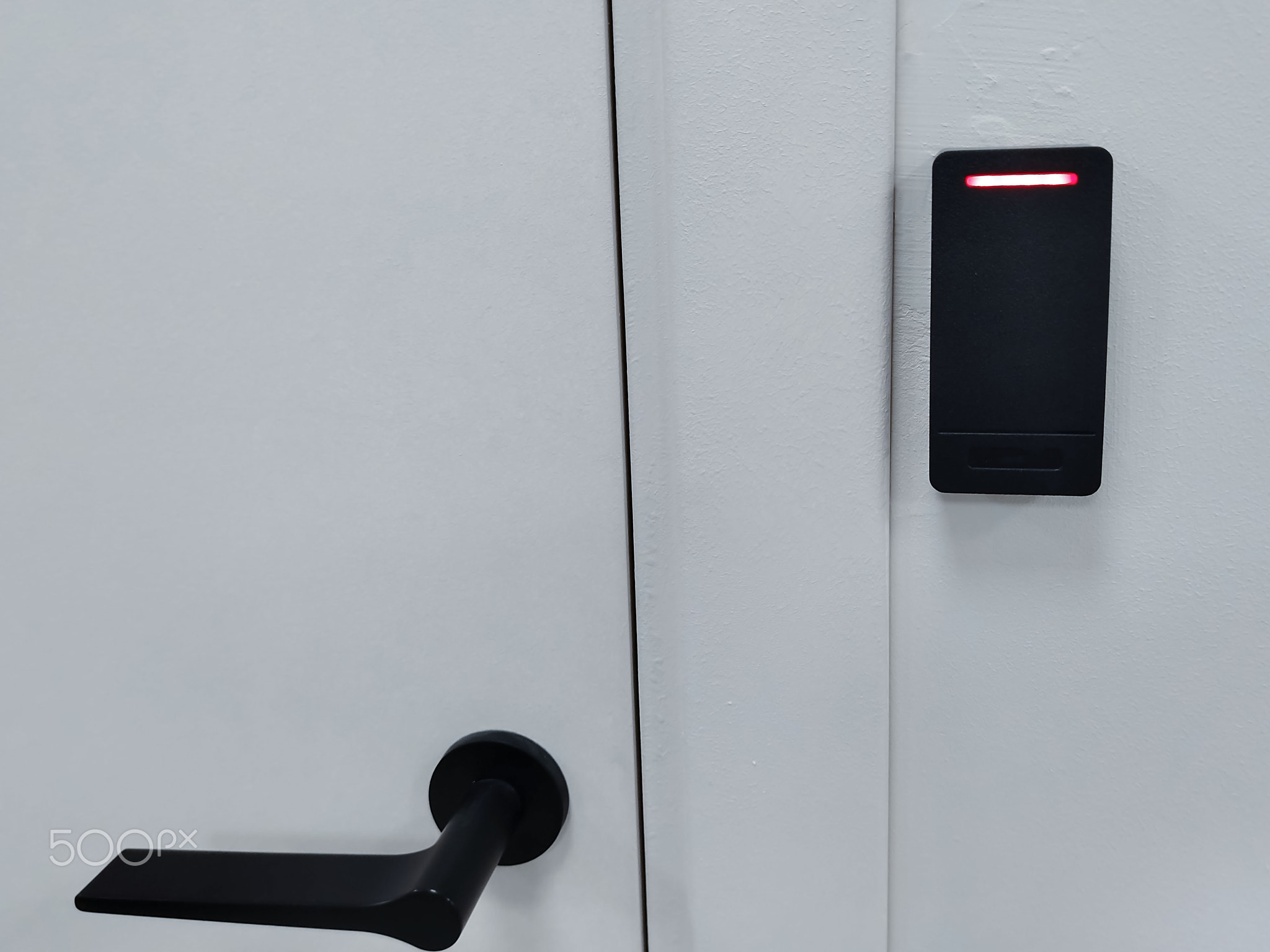 Modern door handle and electronic access control system mounted on a white wall, featuring a red