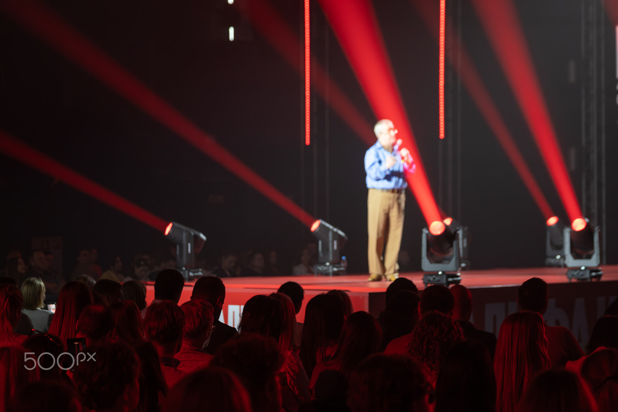 Keynote speaker on stage presenting to large audience at conference with dramatic red lighting