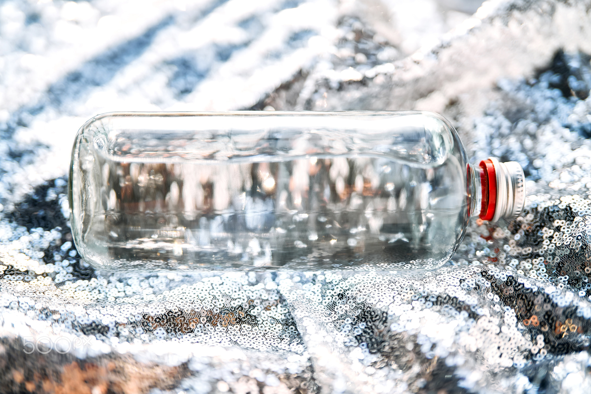 Glass bottle with drinking water reflecting sparkling sequins