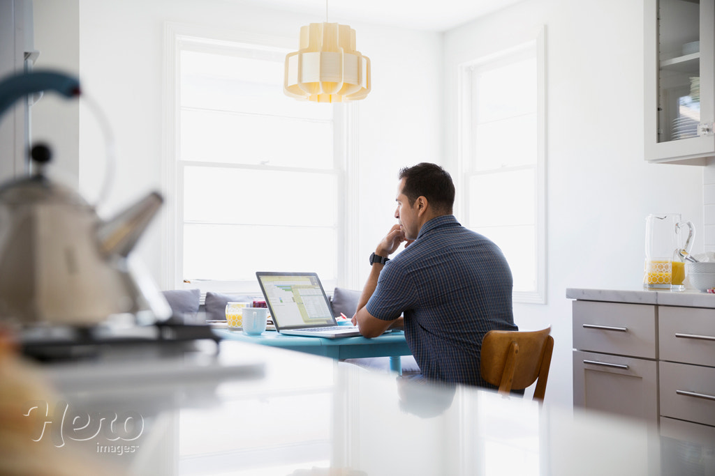 Serious brunette man using laptop at kitchen table