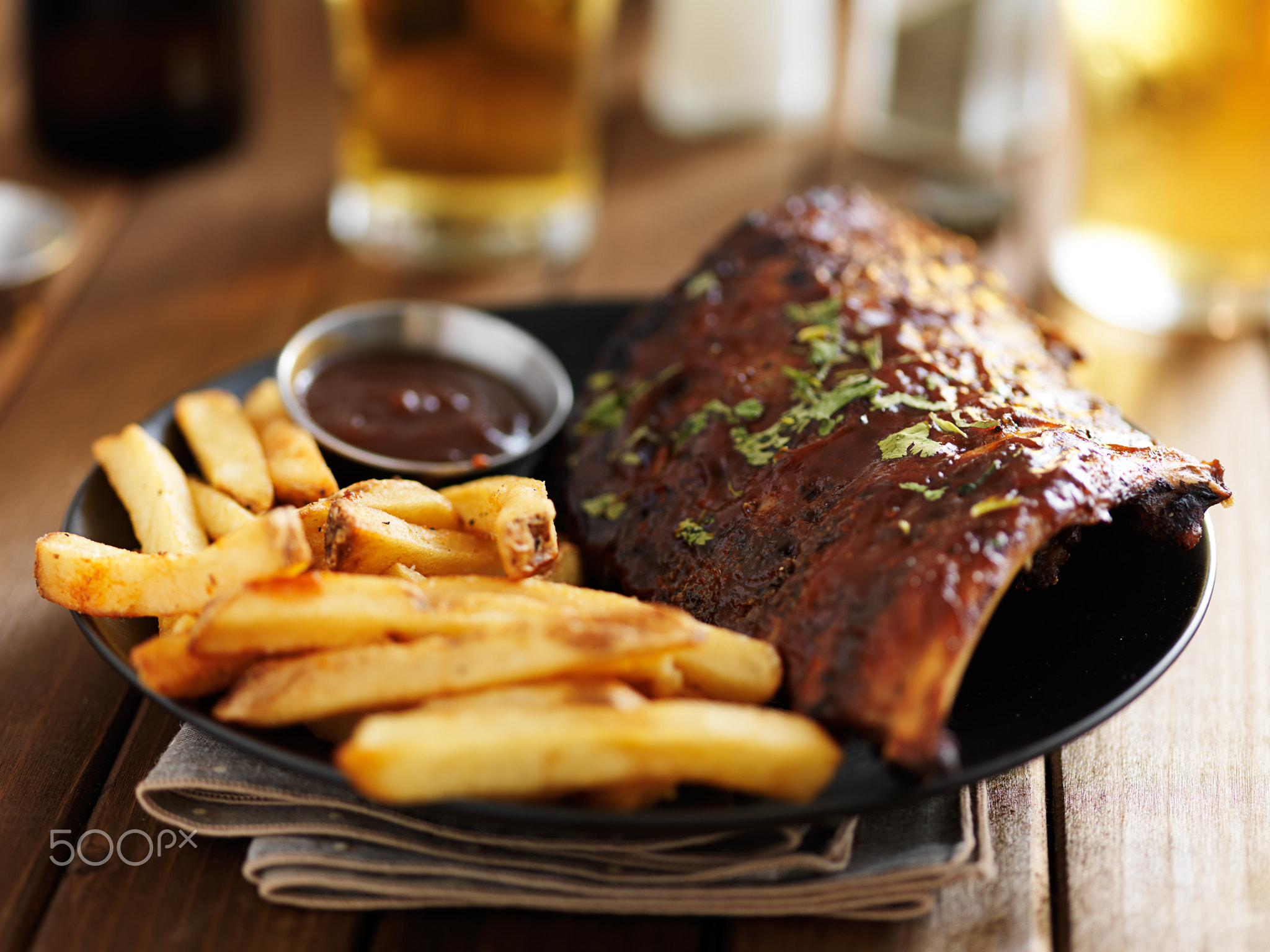 plate of barbecue ribs and fries on wooden table with beer in the background