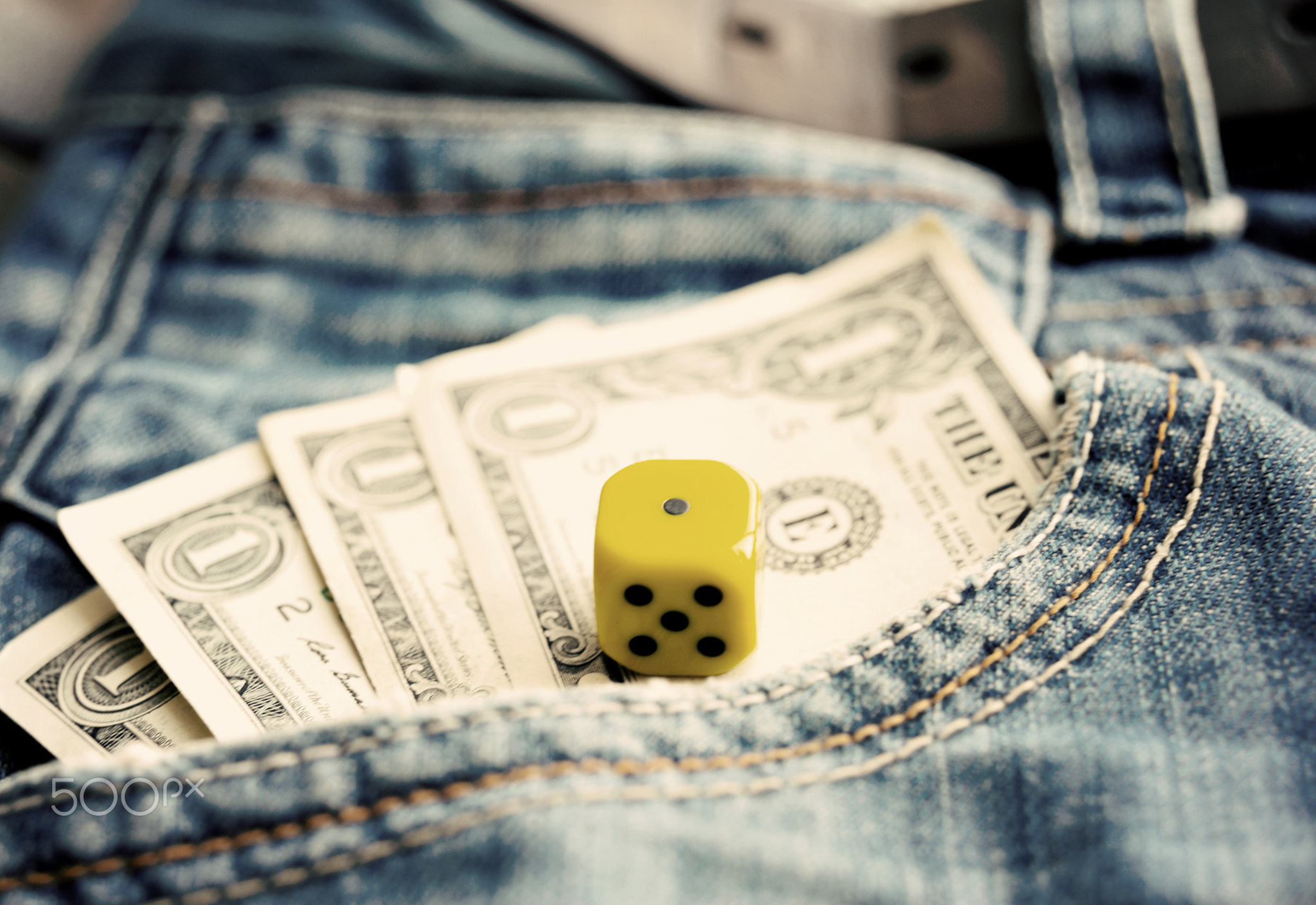 One dollar in pocket denim and a dice close up