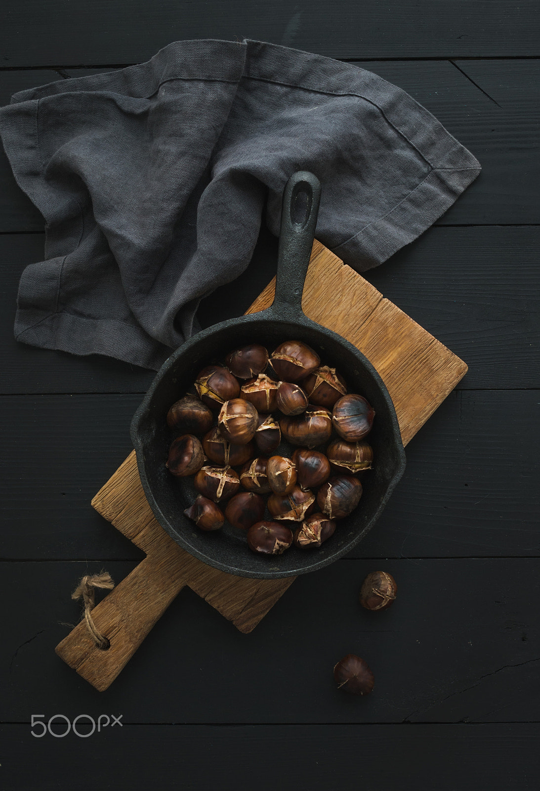 Nikon D610 + ZEISS Distagon T* 35mm F2 sample photo. Roasted chestnuts in iron skillet pan on rustic wooden board over black table background, top view. photography
