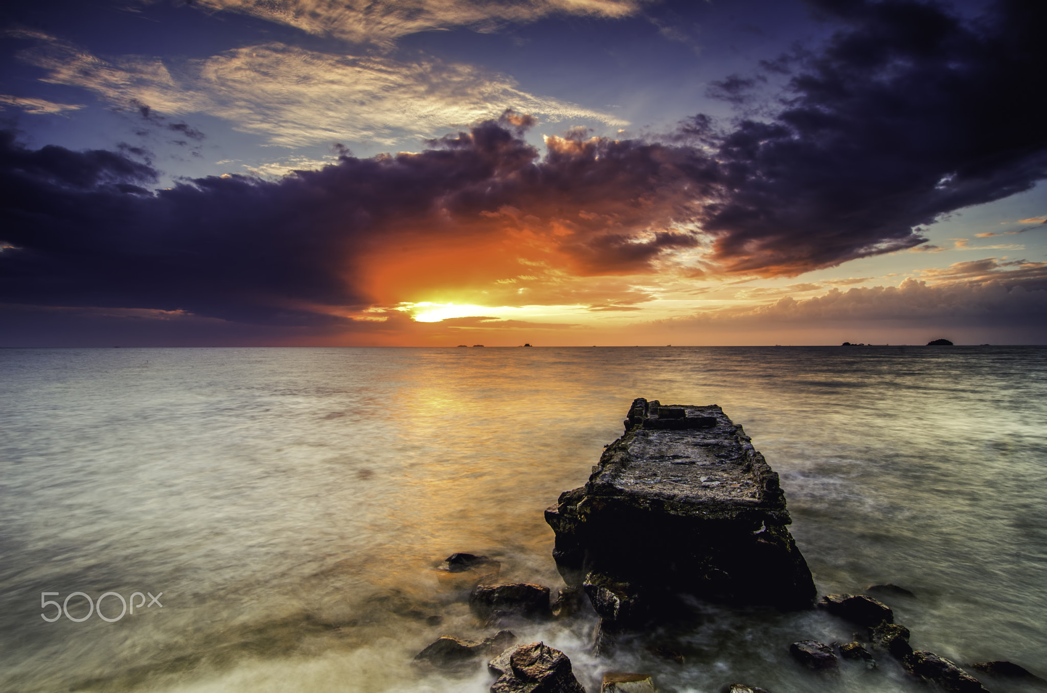 beautiful sunset at the coastline with concrete structure on the beach, dramatic clouds and ray of l