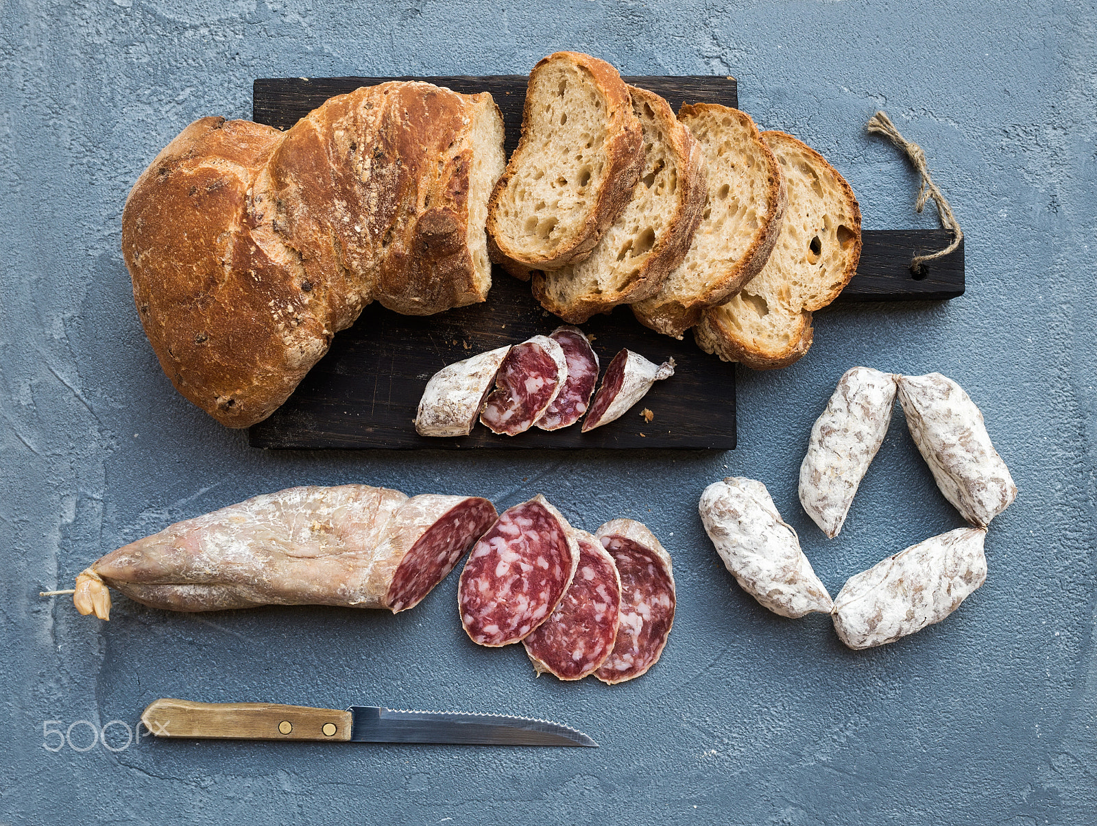Nikon D610 + ZEISS Distagon T* 35mm F2 sample photo. Wine snack set. italian slami sausages and rustic bread on dark wooden board over a rough grey-blue  photography