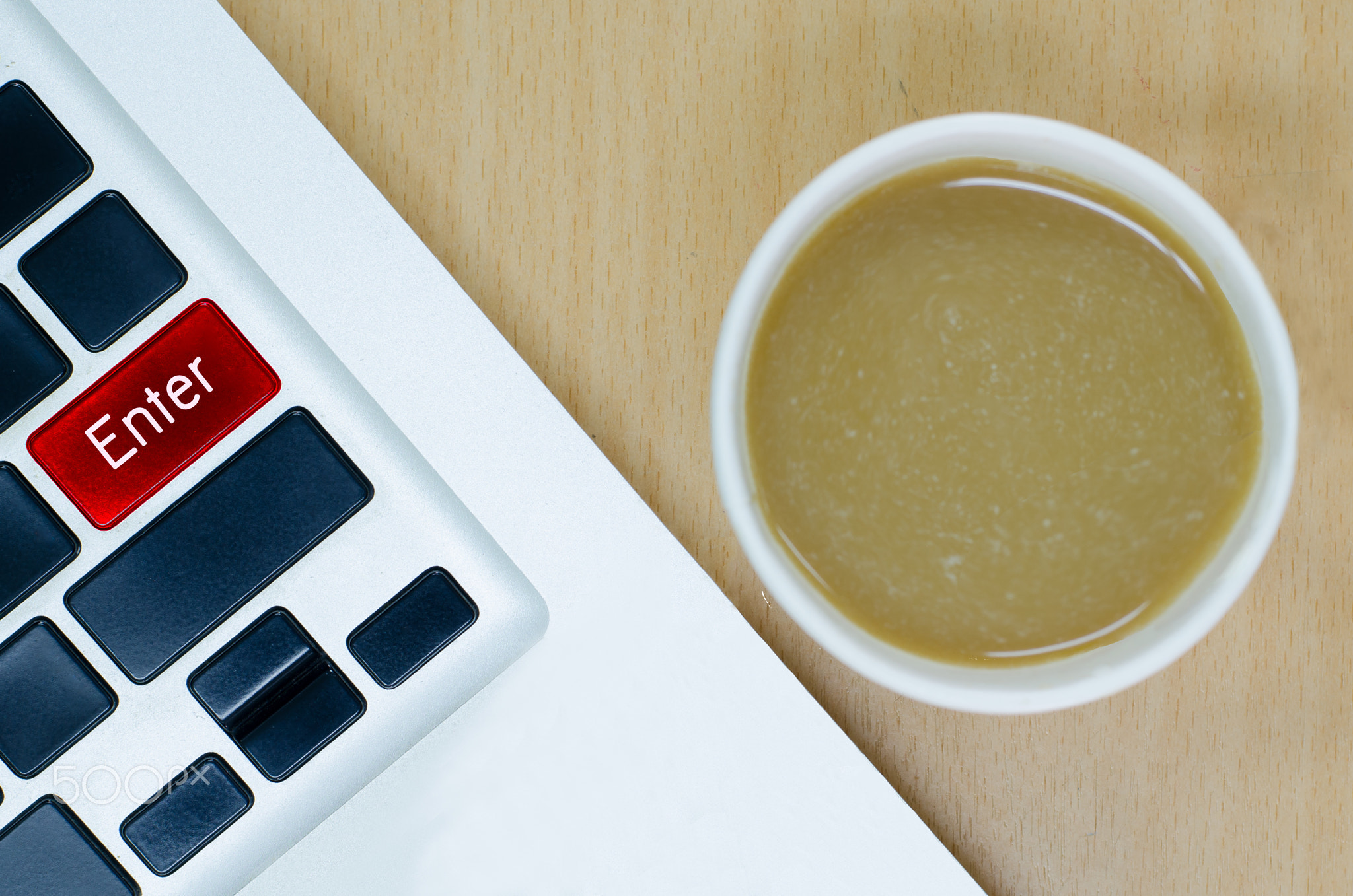 Laptop keyboard with coffee paper cup on wooden desk, enter keyp