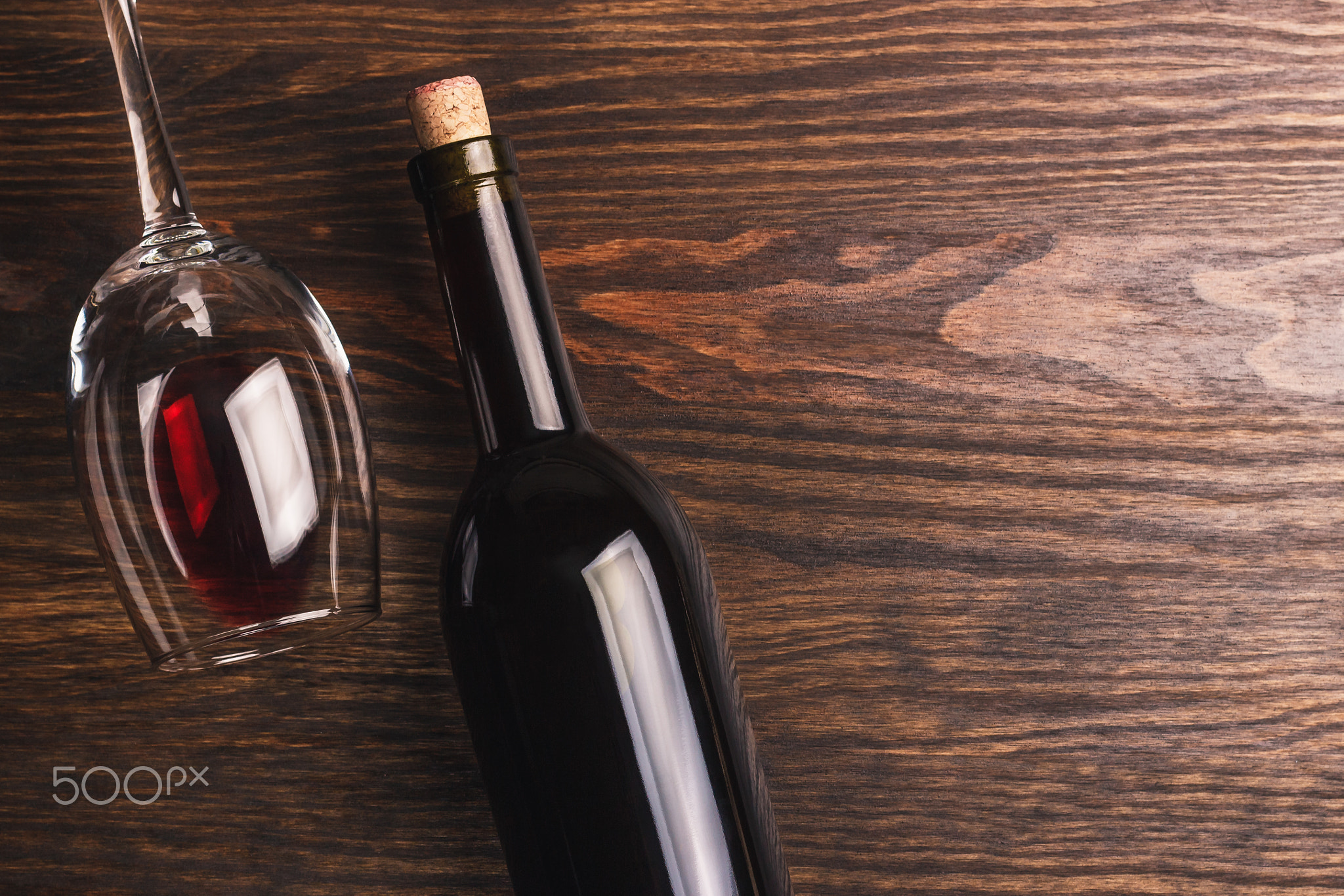 Glass with wine and bottle with cork, wooden background