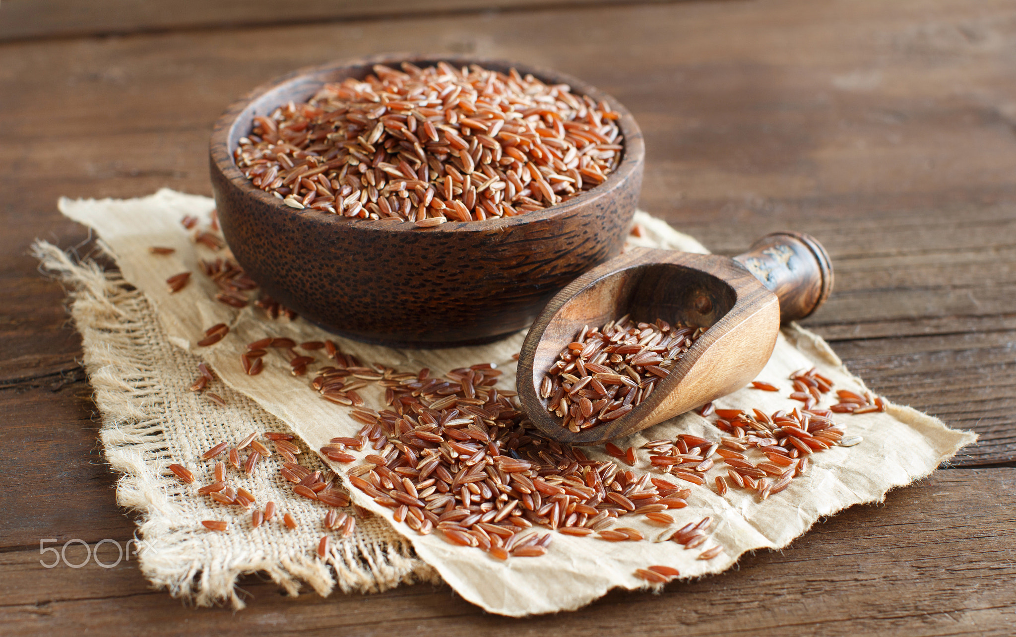 Uncooked Red rice in a bowl with a wooden spoon