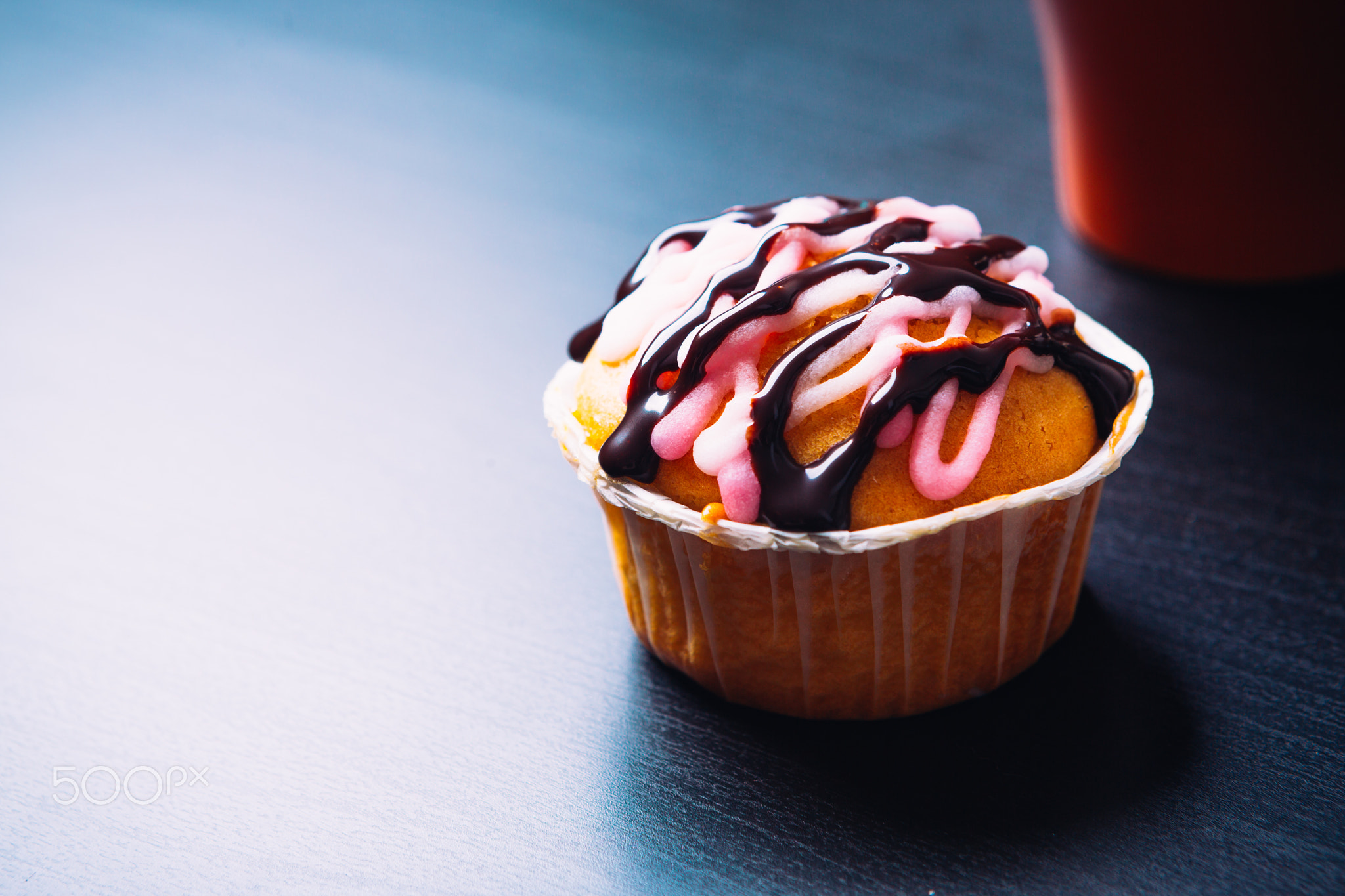 cupcake with pink frosting and red cup on a wooden background