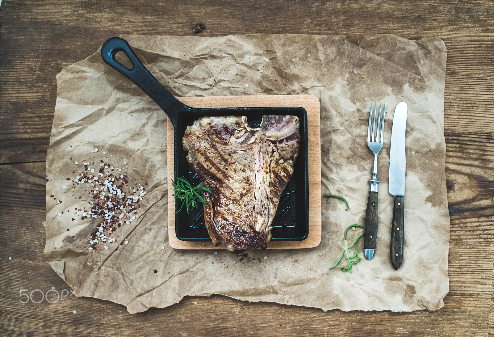Nikon D610 + ZEISS Distagon T* 35mm F2 sample photo. Cooked meat t-bone steak in grilling pan with spices and fresh rosemary on oily craft paper over... photography