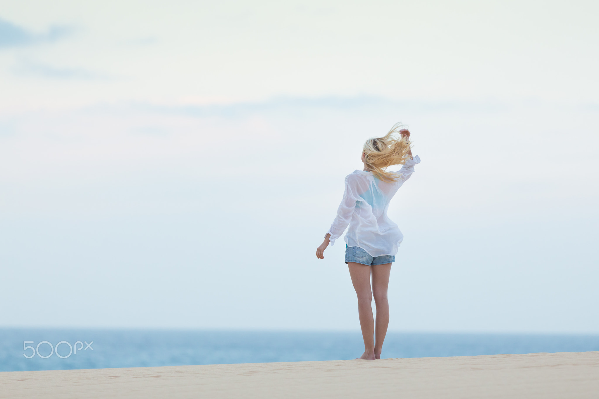 Woman on sandy beach in white shirt in morning.