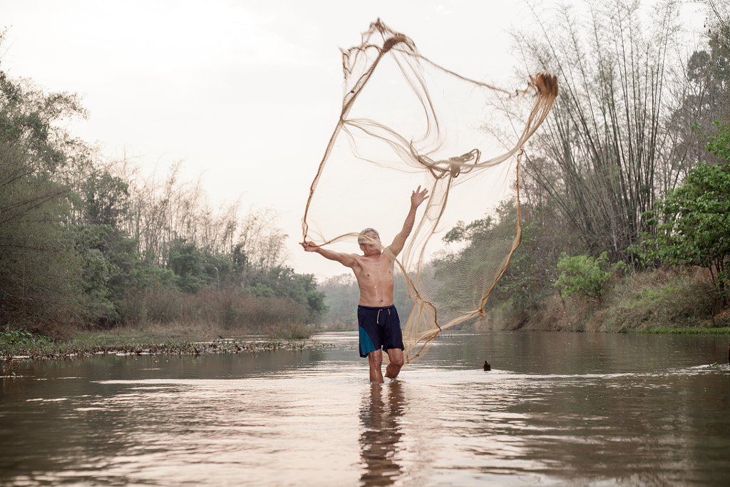 Asian old fisherman casting his fishnet in river by Panuwat Phengkhumphu on 500px.com