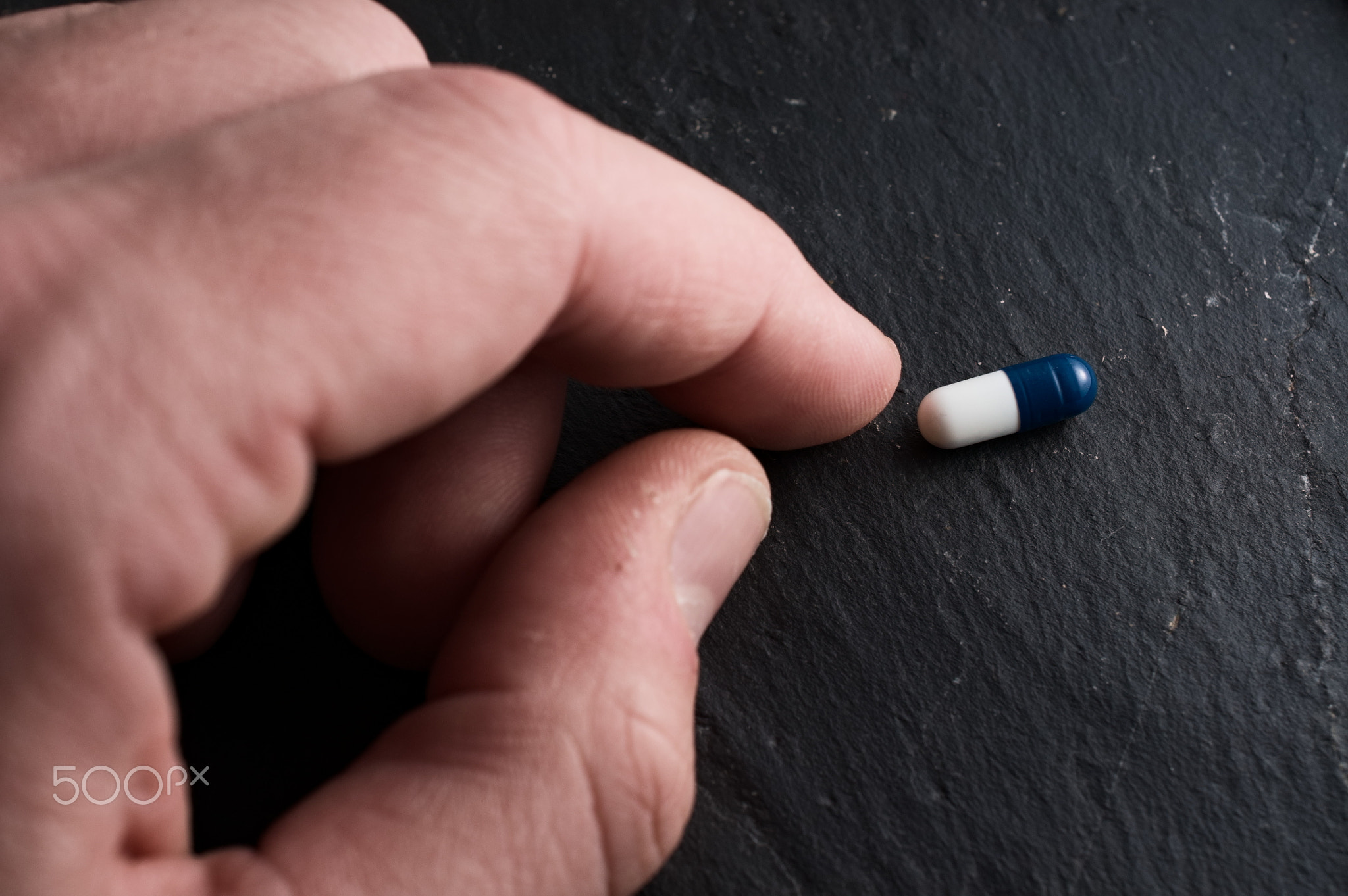 Adult model male hand reaching for blue and white pill