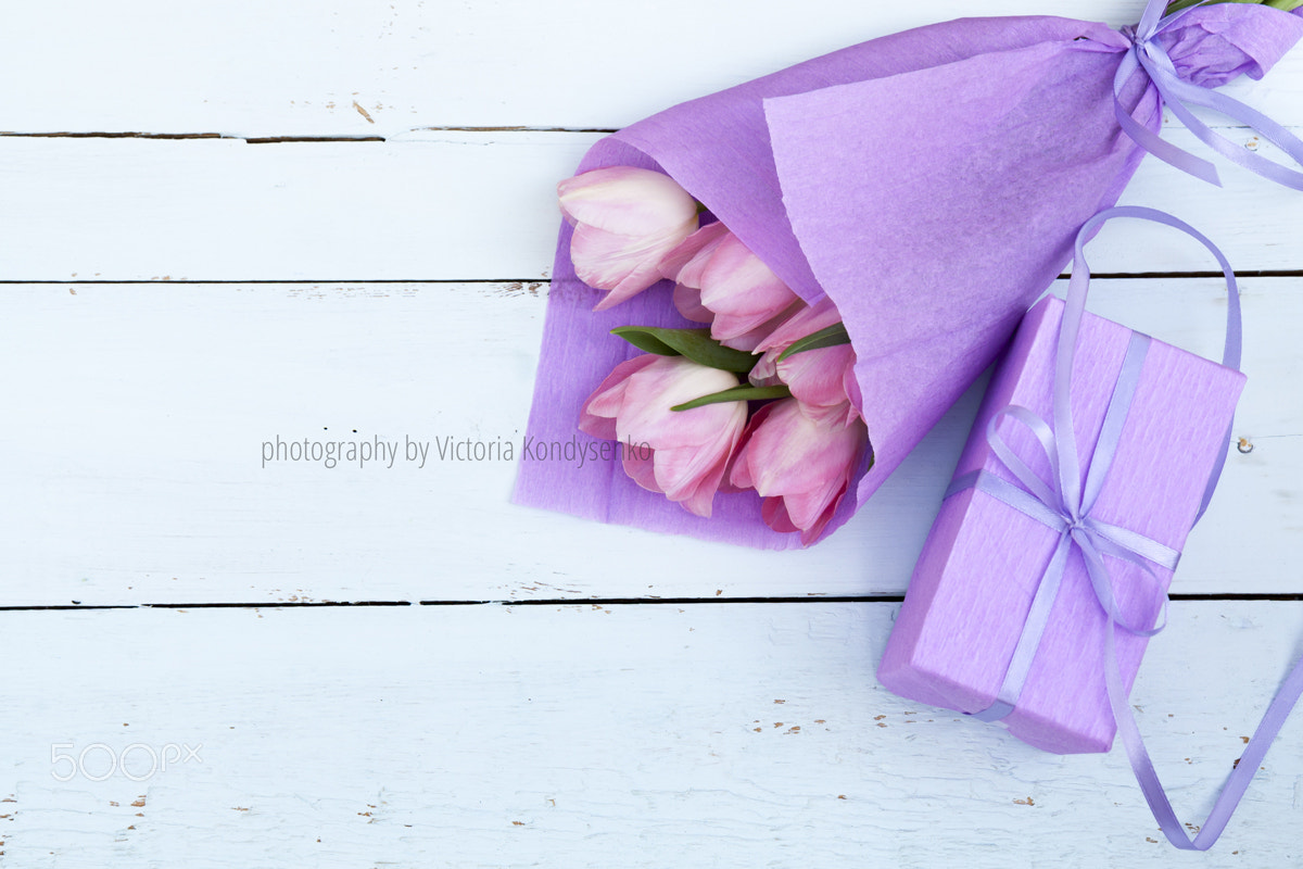Beautiful bouquet of pink tulips in violet paper and gift on lig
