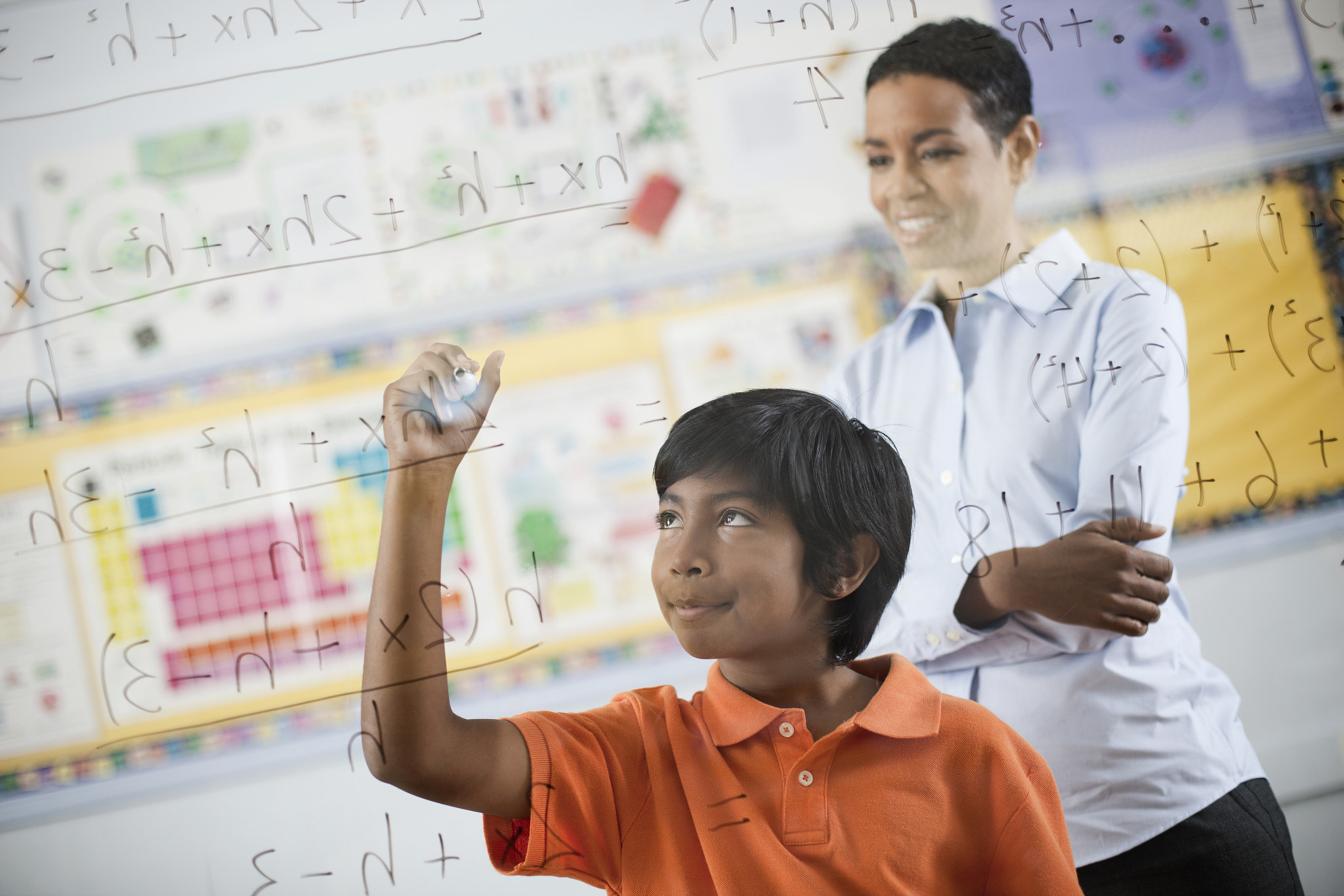 A student writing formula and equations on a clear perspex board, with pens. 