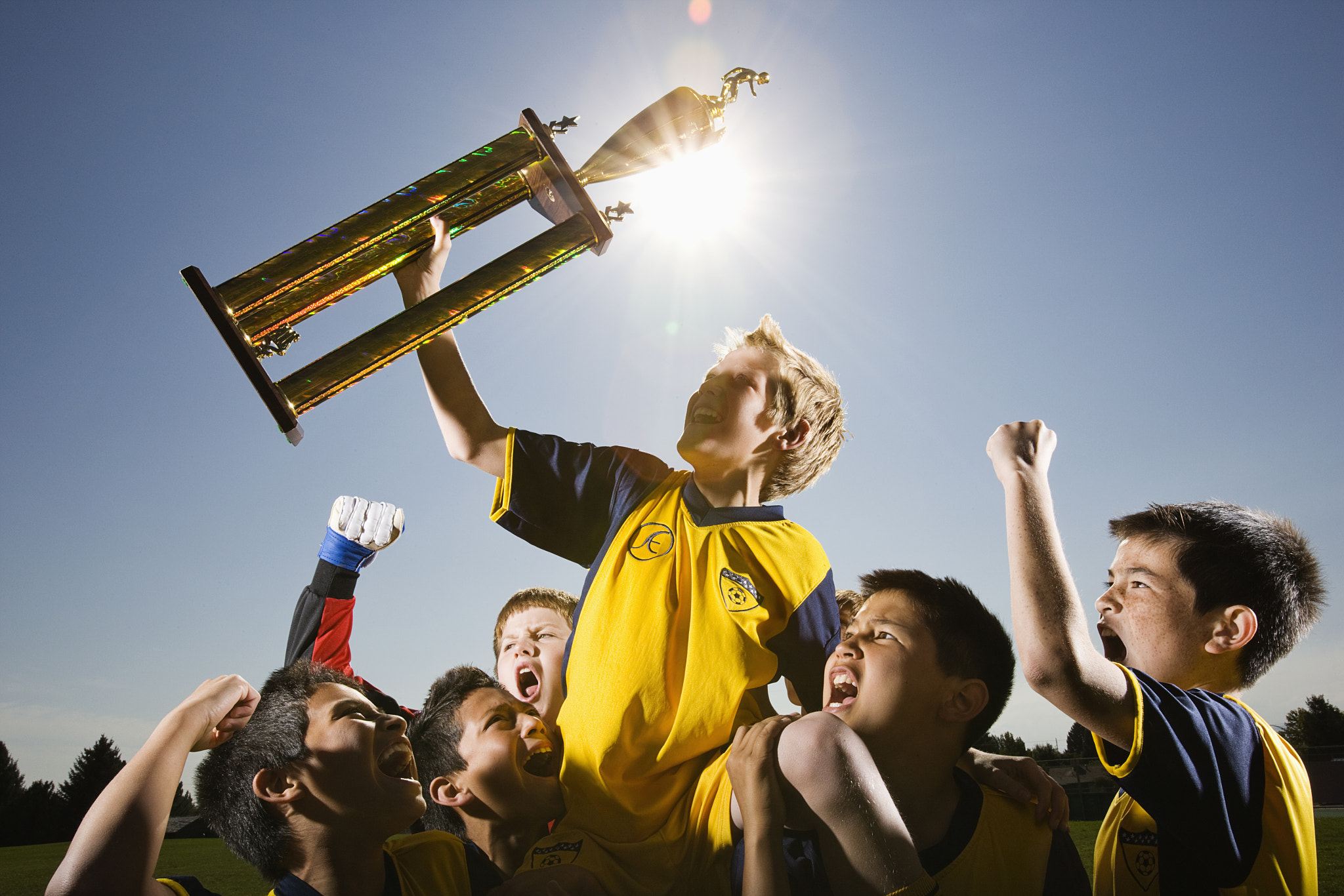 A group of boys in soccer team shirts holding a trophy and celebrating a win.