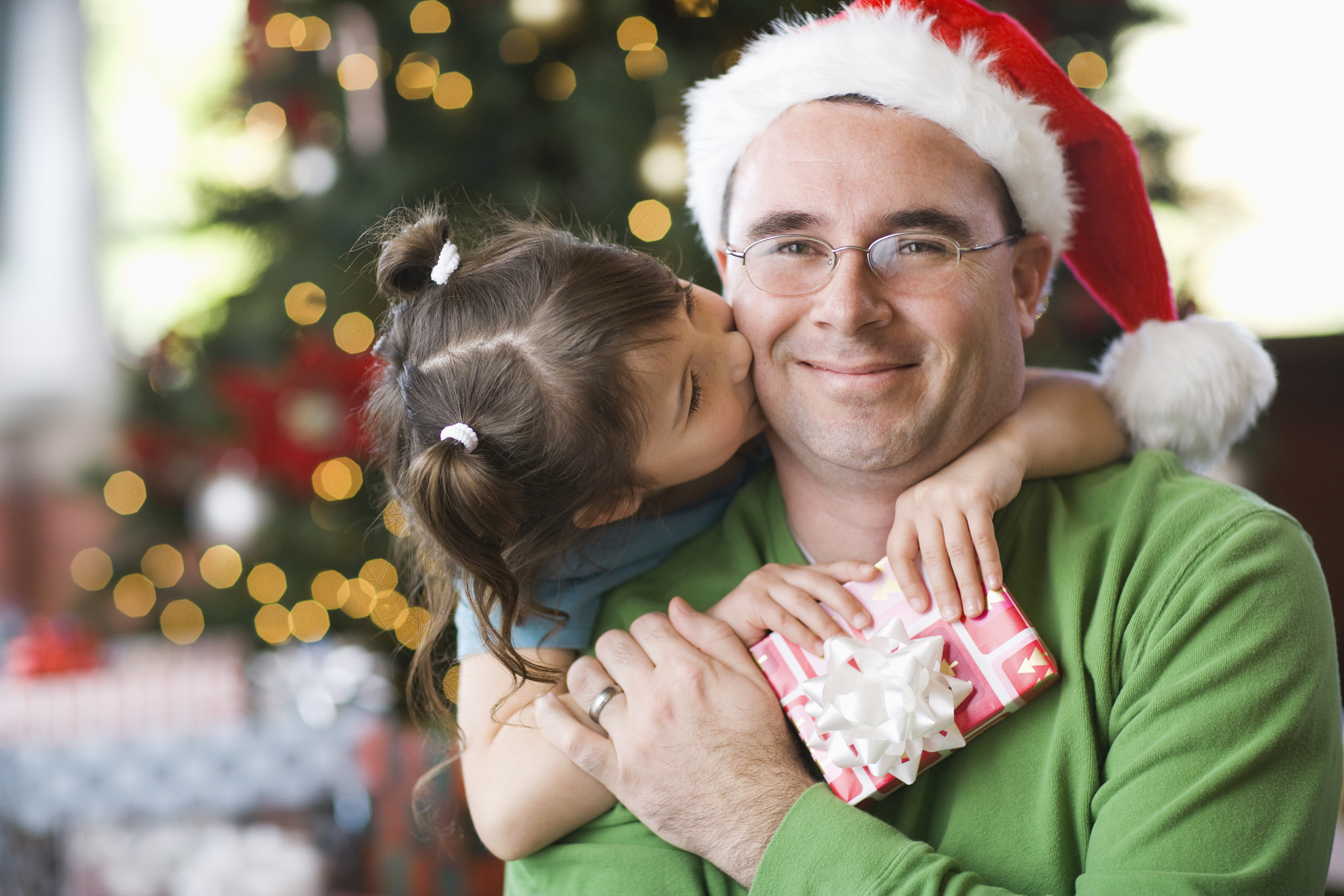 A man and a girl, father and daughter, hugging and exchanging presents by a Christmas tree.
