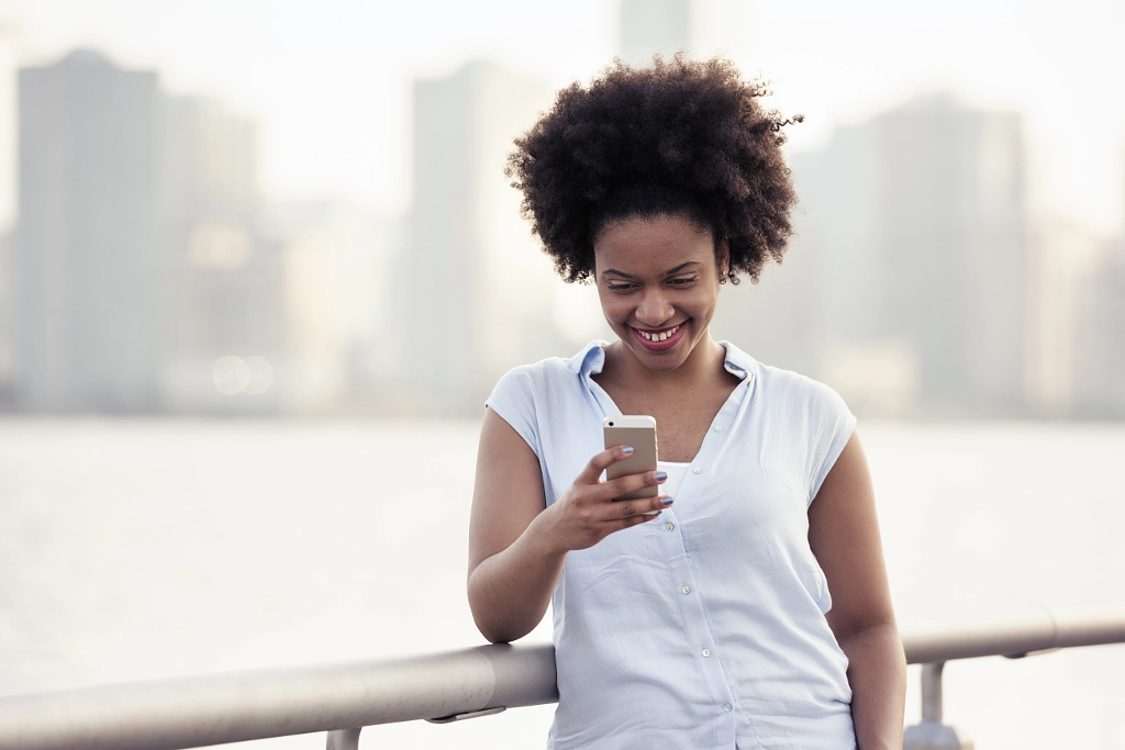 A woman leaning on a waterfront rail checking her cell phone by Mint Images on 500px.com