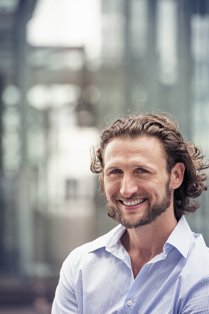 A man with curly hair and a beard on a city street. by Mint Images on 500px.com