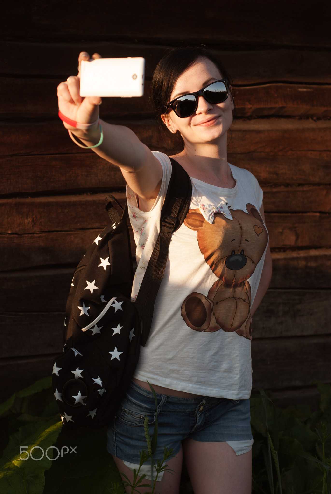 Charming girl in sunglasses making a self-portrait with funny face on your smartphone