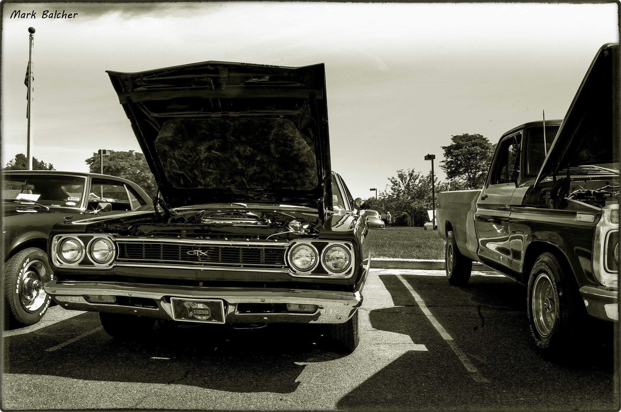 Pentax K-x sample photo. A black and white shot of the plymouth gtx, with it's hood up and a ford pick up next to it. photography