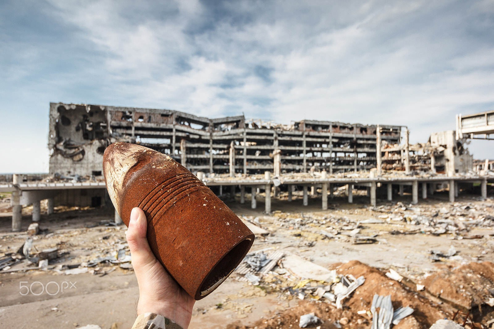 Canon EF-S 10-18mm F4.5–5.6 IS STM sample photo. Unexploded 120 mm shell in hand with airport ruins photography