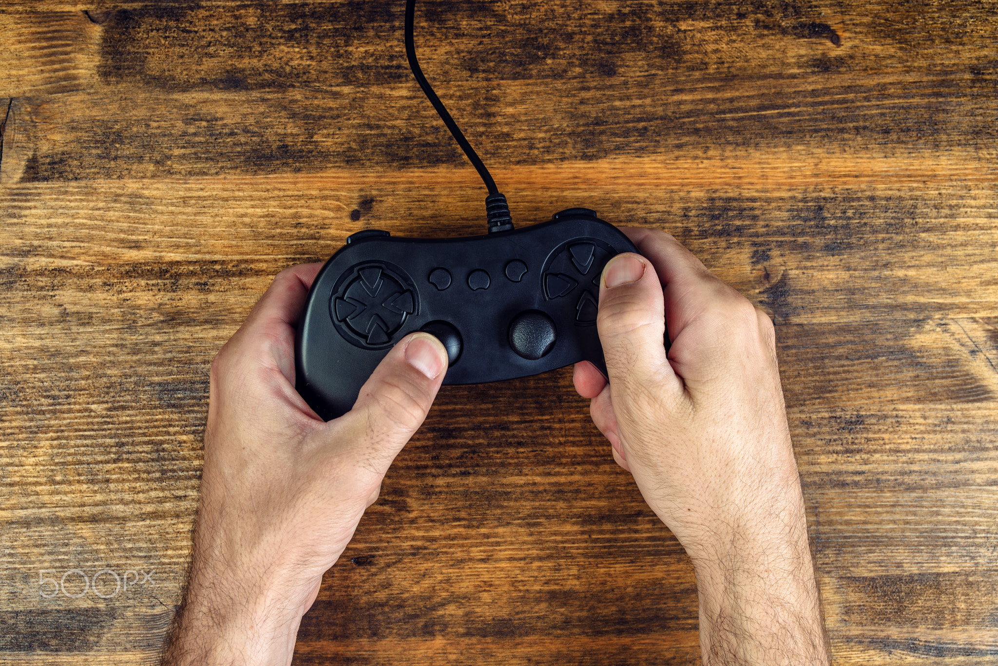 Male gamer using gamepad controller on wooden desk, top view