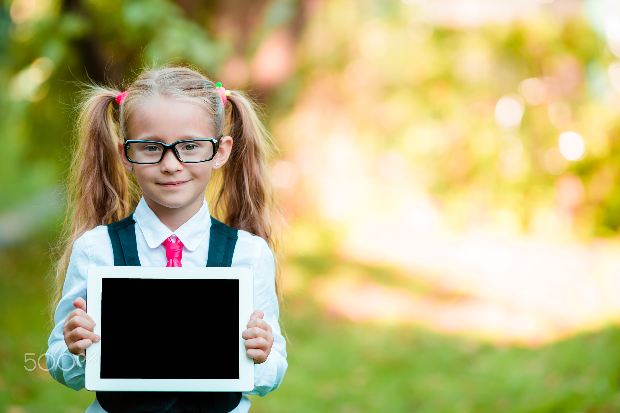 Adorable little girl holding tablet PC outdoors in autumn sunny day