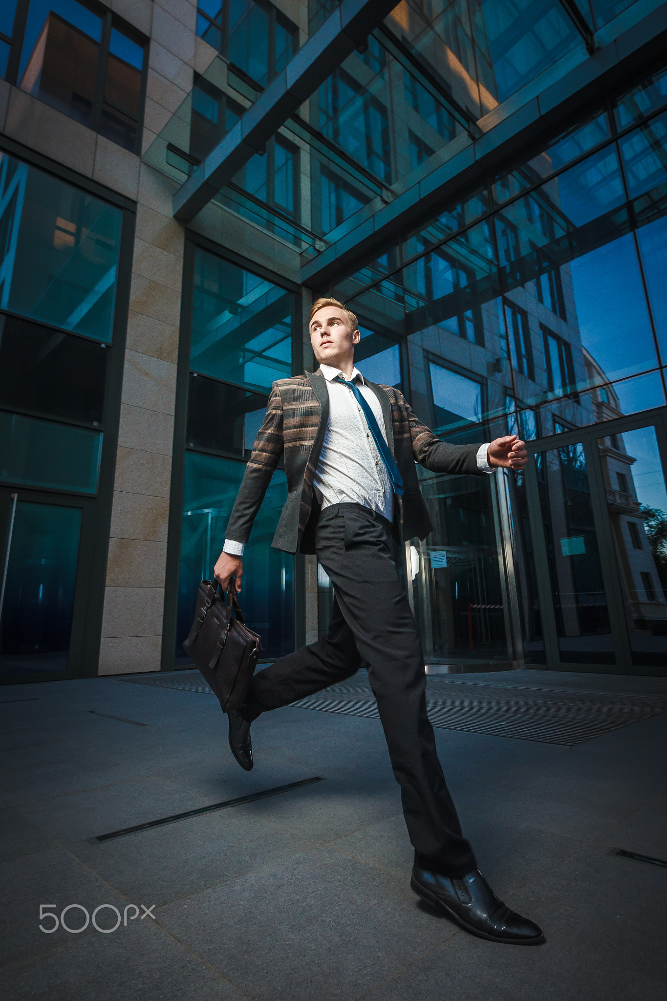 Young handsome successful stylish businessman running near modern office