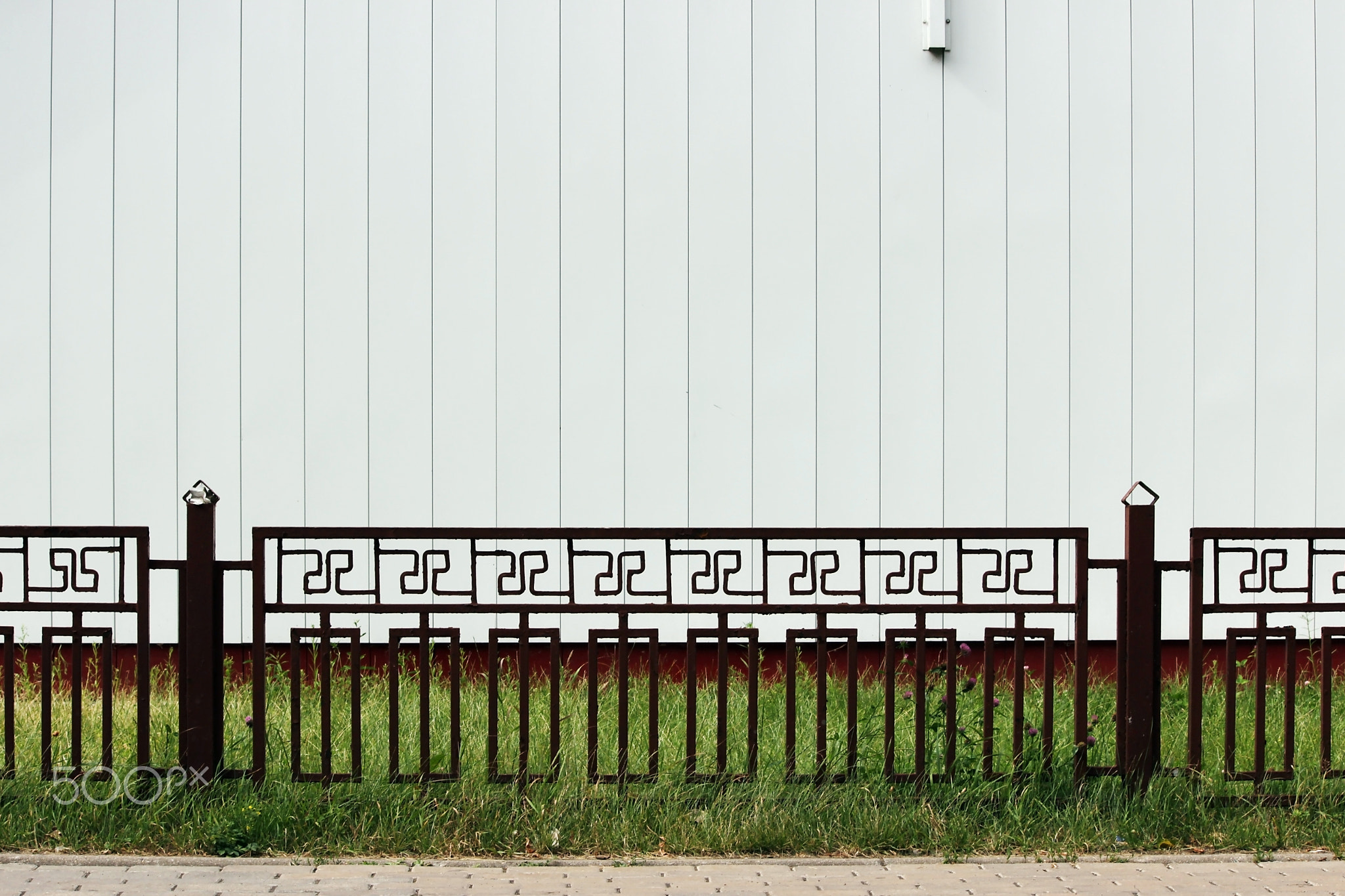 red metal fence and green grass on a background of white walls